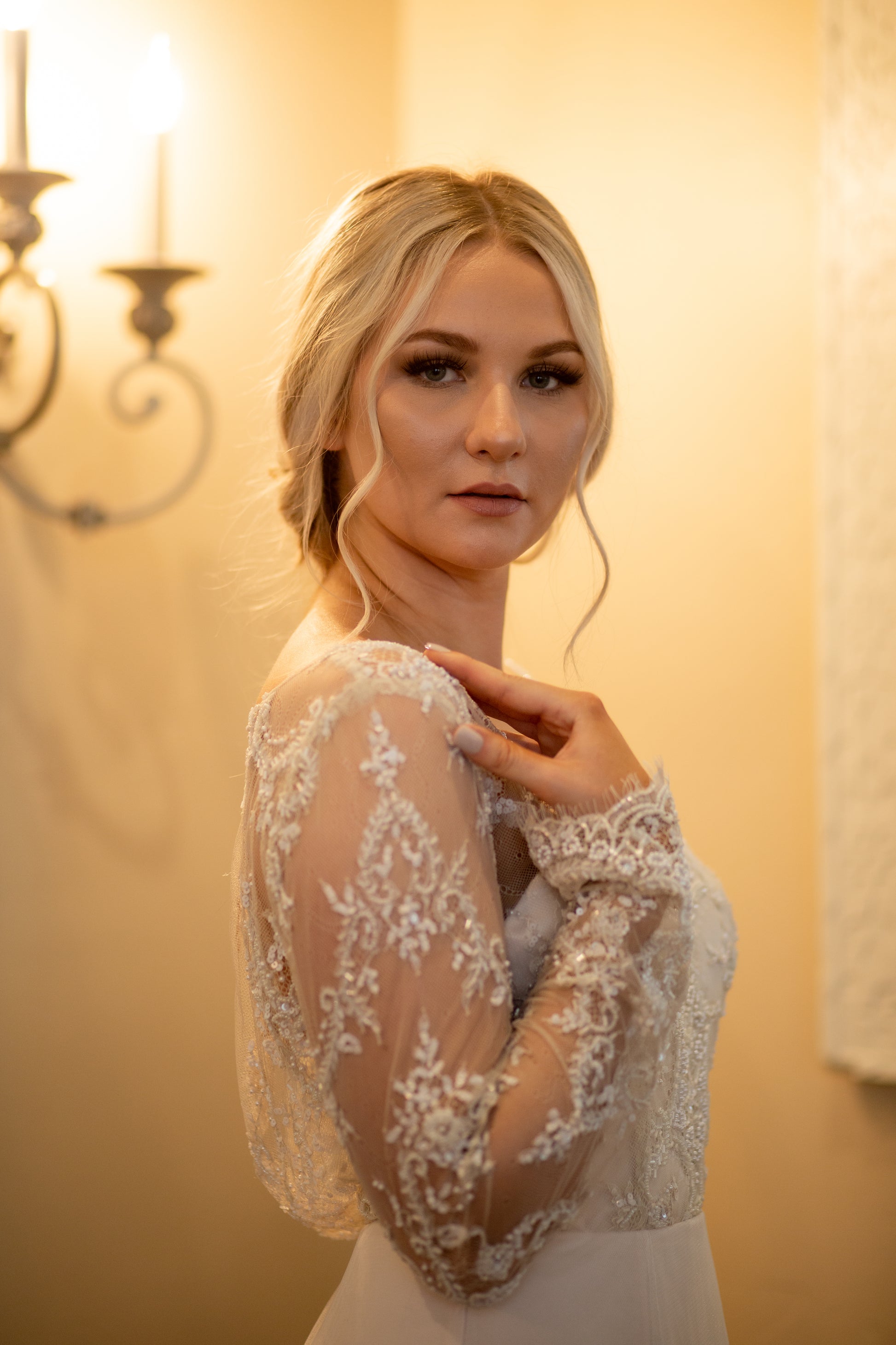 Side profile of bride in Eivissa gown, with her hand placed on her shoulder you can see the sheer lace sleeve and the rise and fall of the beaded pattern.