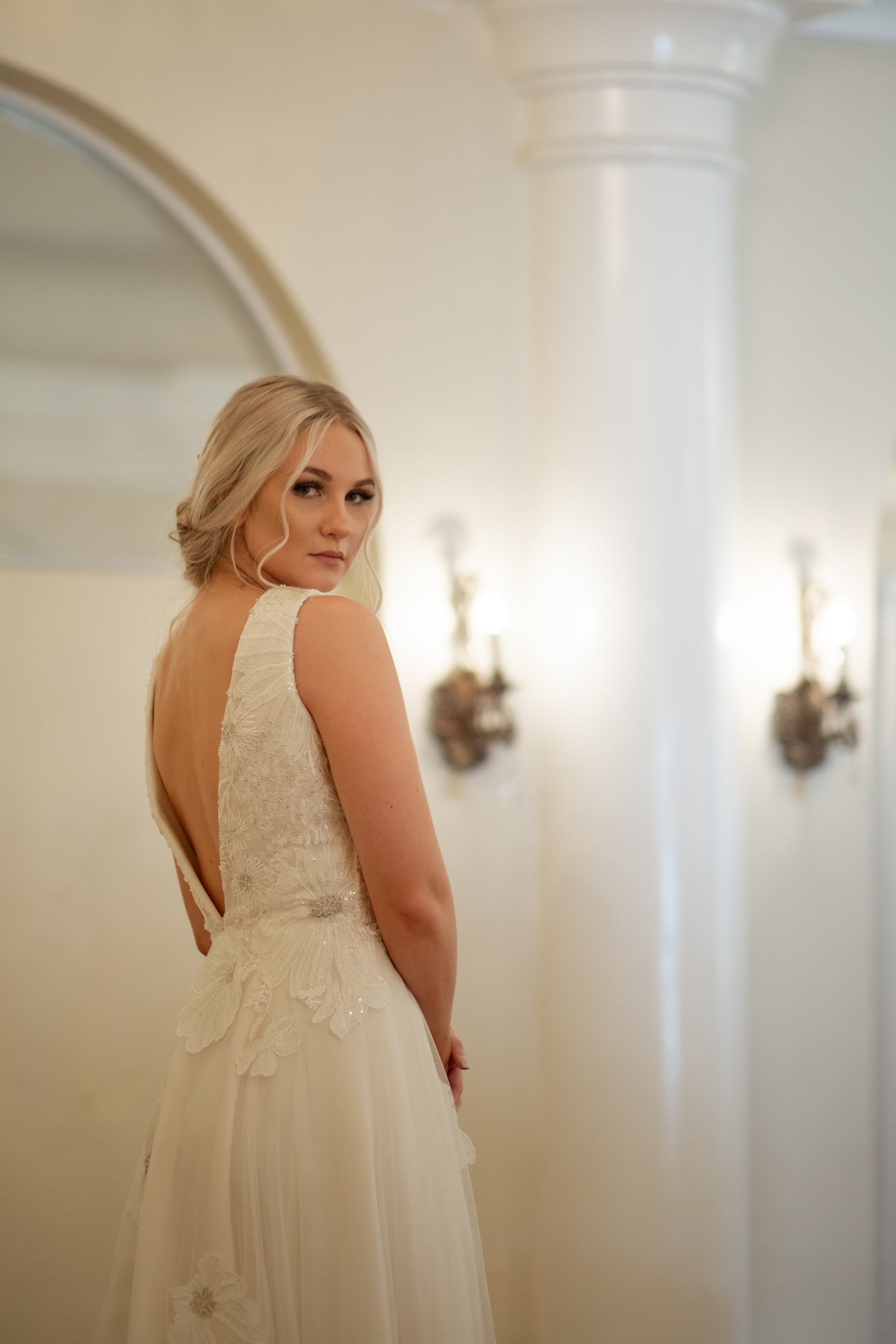 The poppy gown worn by a bride looking over her sholder; showing the gown from a ¾ back view. The low v neck and lace bodice is the focus.