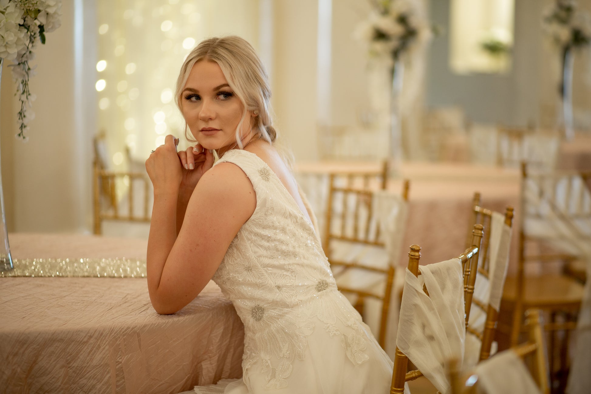 A bride wears the Poppy gown and sits at a table leaning forward. You can see the structured lace bodice and the way the lace trails down into the tulle skirt.
