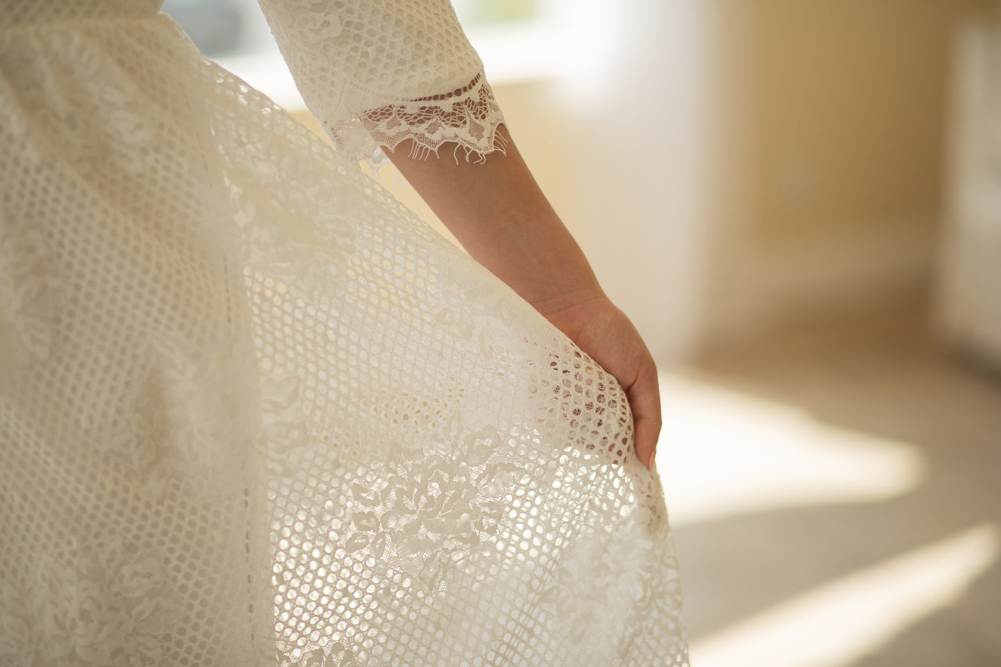 Detailed close-up of the Avabelle gown’s lace and three-quarter-length sleeves, revealing the intricate rose lace, cording, and eyelash trim along the scalloped edges.