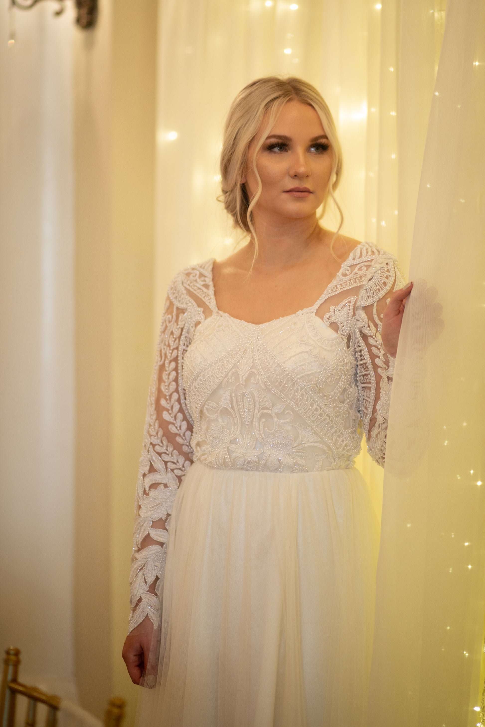 Close up of a bride wearing the farrah gown. Shows off the front bodice, flowy skirt and long sleeves.