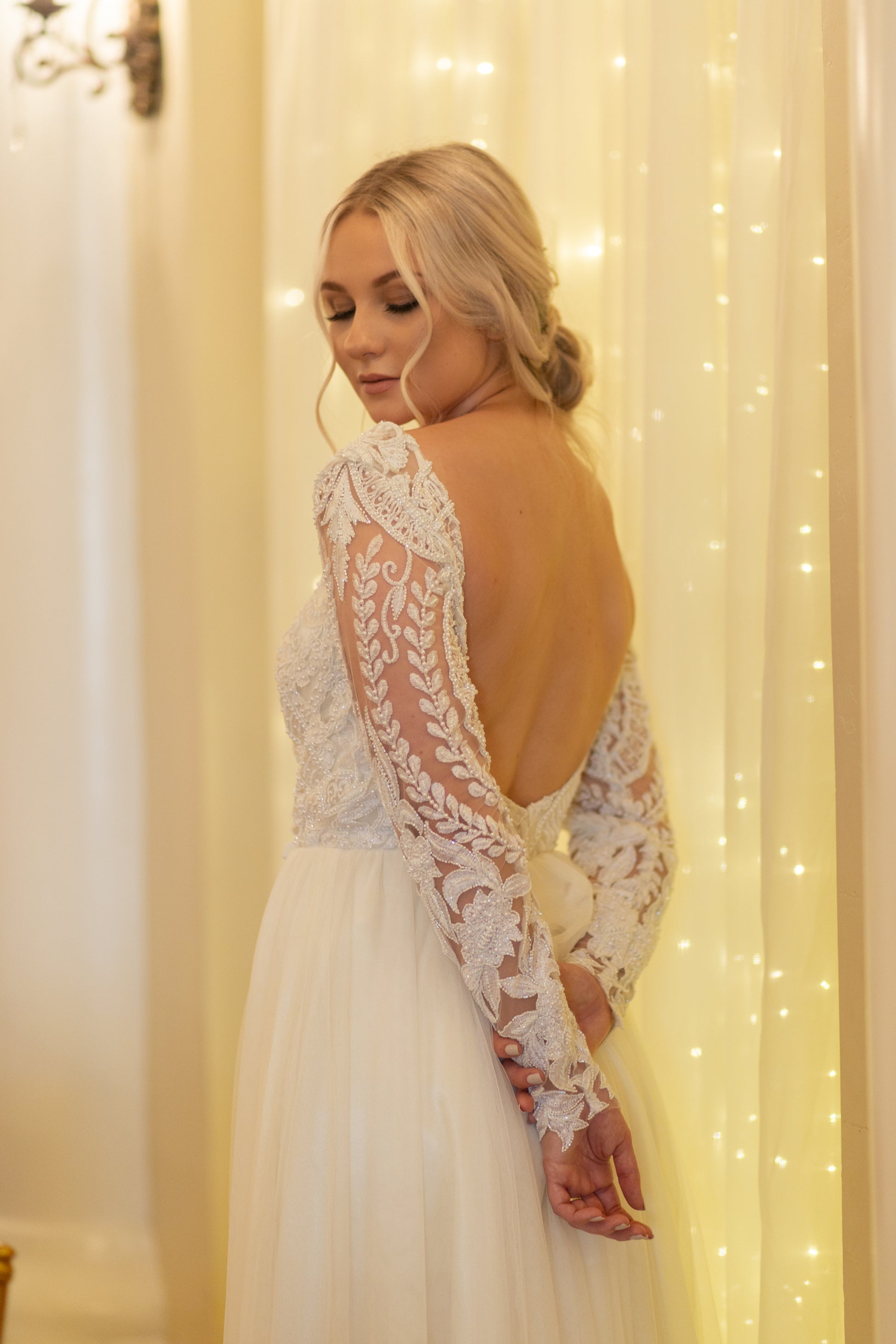 Bride looking over shoulder to show back square neckline and the pattern of the long lace sleeves.