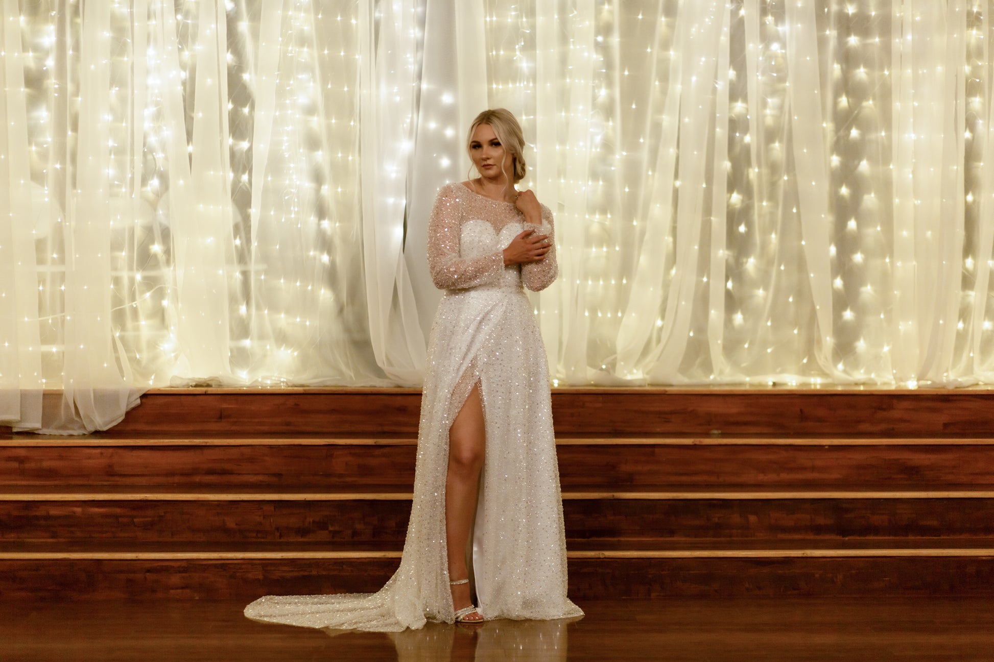 Dramatic image of a bride wearing the Faelynn gown. Shown from the front it emphasizes the faux wrap skirt with her right knee popping forward and through while the train sweeps to the side.