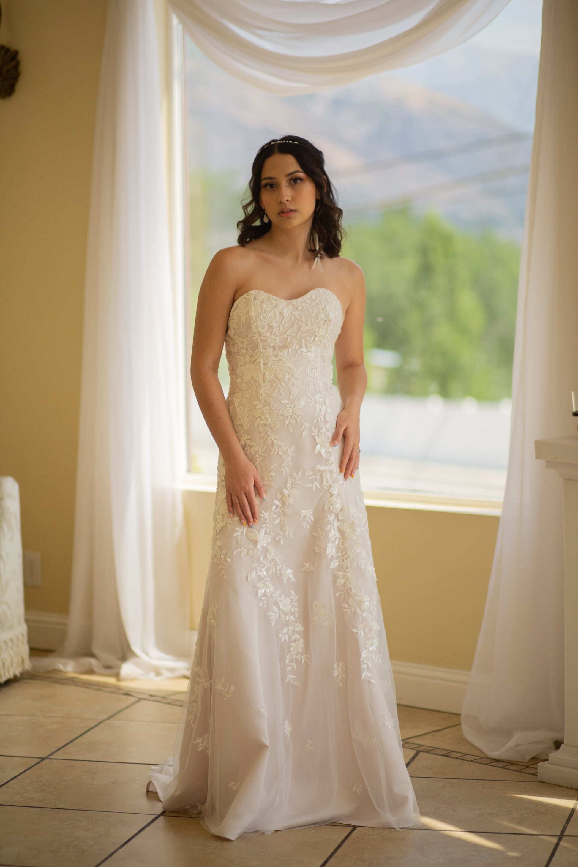 A full length photo of the front of the Sawyer gown, a bride wears it as hit highlights the trumpet shape and beaded lace that fades as you get to the hem.