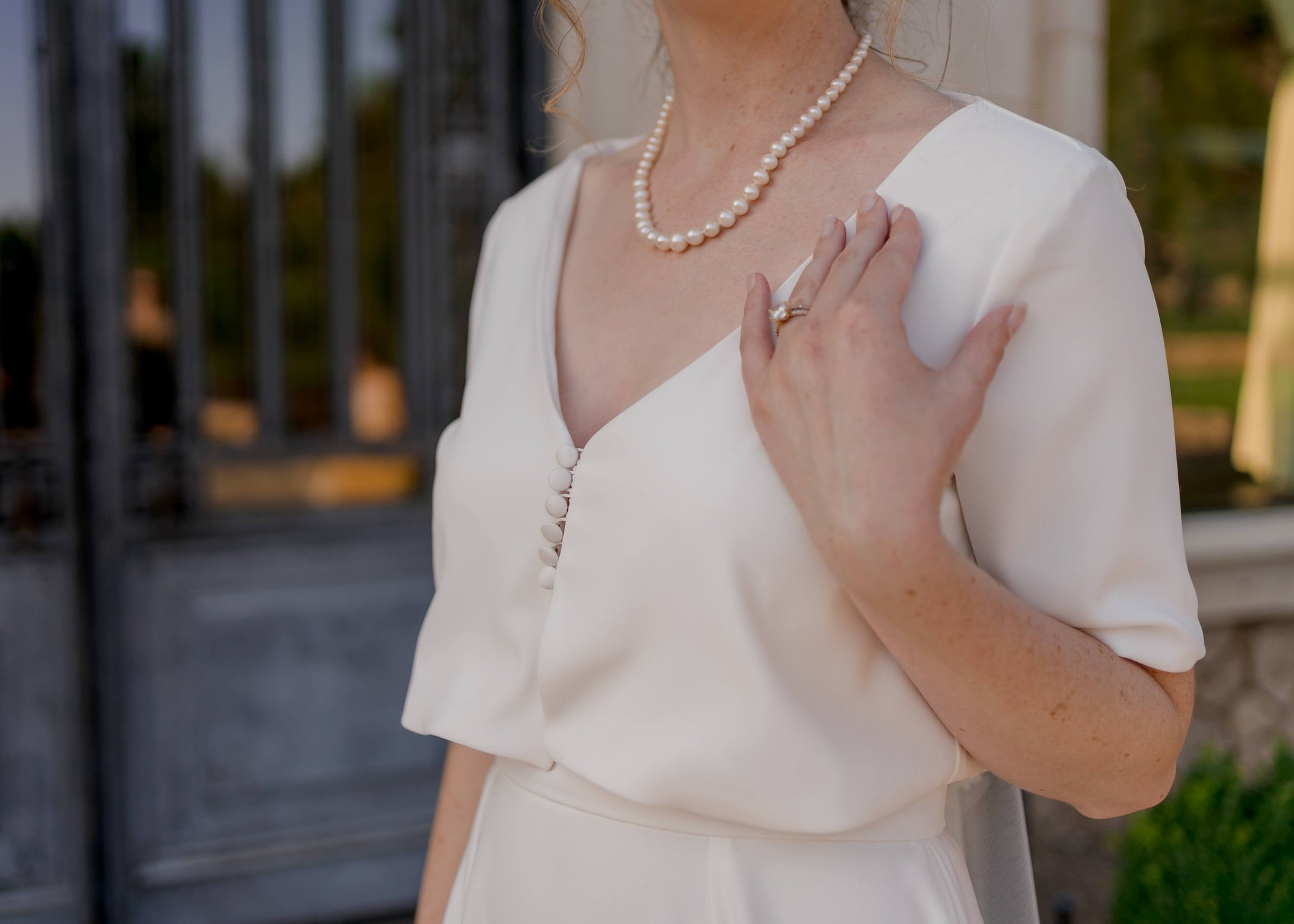 Detailed close-up of a bride wearing the Cassie bridal set, focusing on the cropped bodice’s soft V-neckline, short sleeves, and delicate button details.