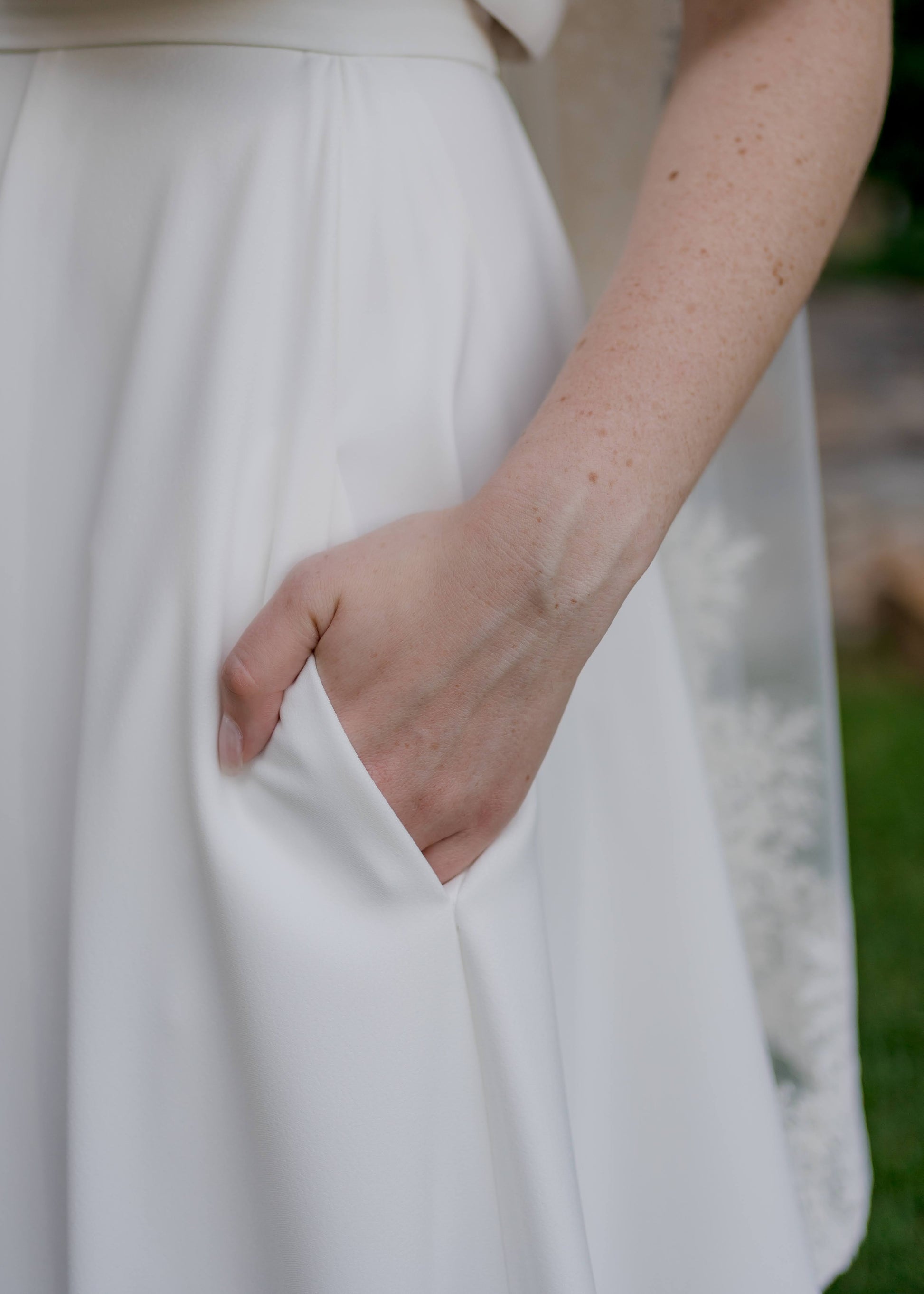 Close-up of the Cassie bridal skirt pocket with the bride’s hand tucked inside, showing the practical hidden detail within the soft A-line silhouette of the stretch crepe fabric.