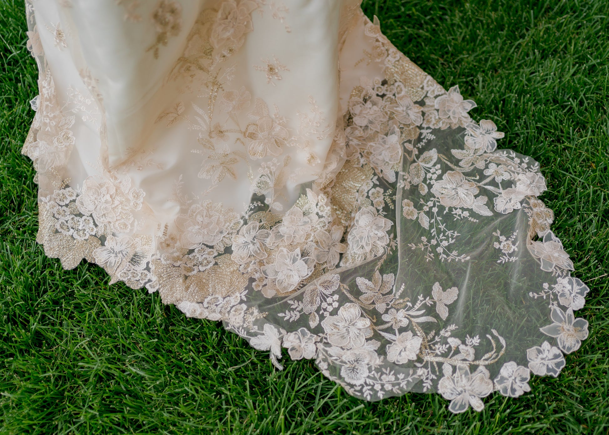 A close up of the 18 inch long train on the Reagan gown; the Champagne and gold 3D floral lace with metallic leaf embroidery lace contrasts against a green lawn.