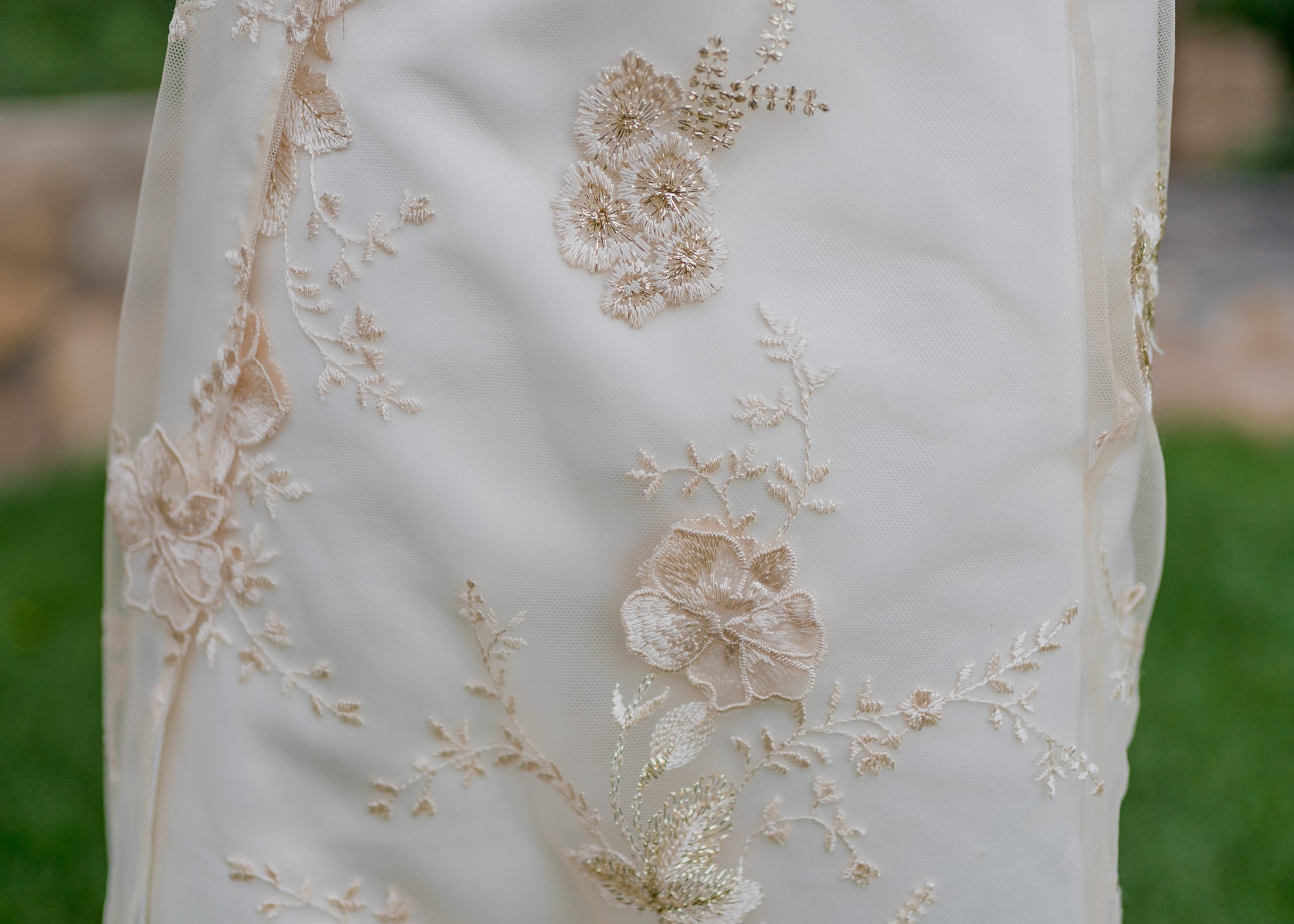 A close up detail shot of the skirt on the Reagan wedding gown; Champagne and gold 3D floral lace with metallic leaf embroidery against ivory satin.