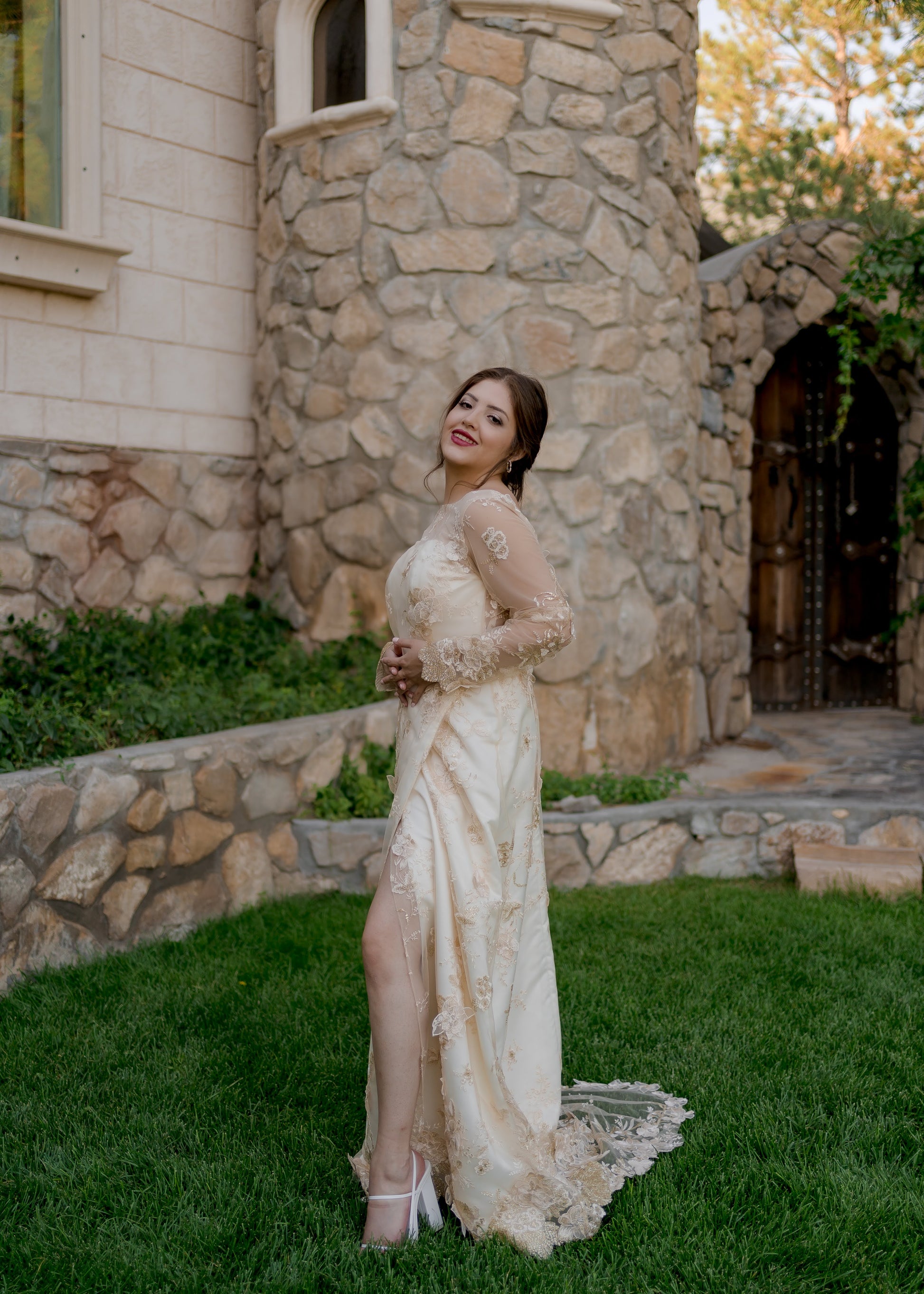 A full length side view of the Reagan wedding gown; a bride wears the gown with her knee popped through the faux wrap skirt.