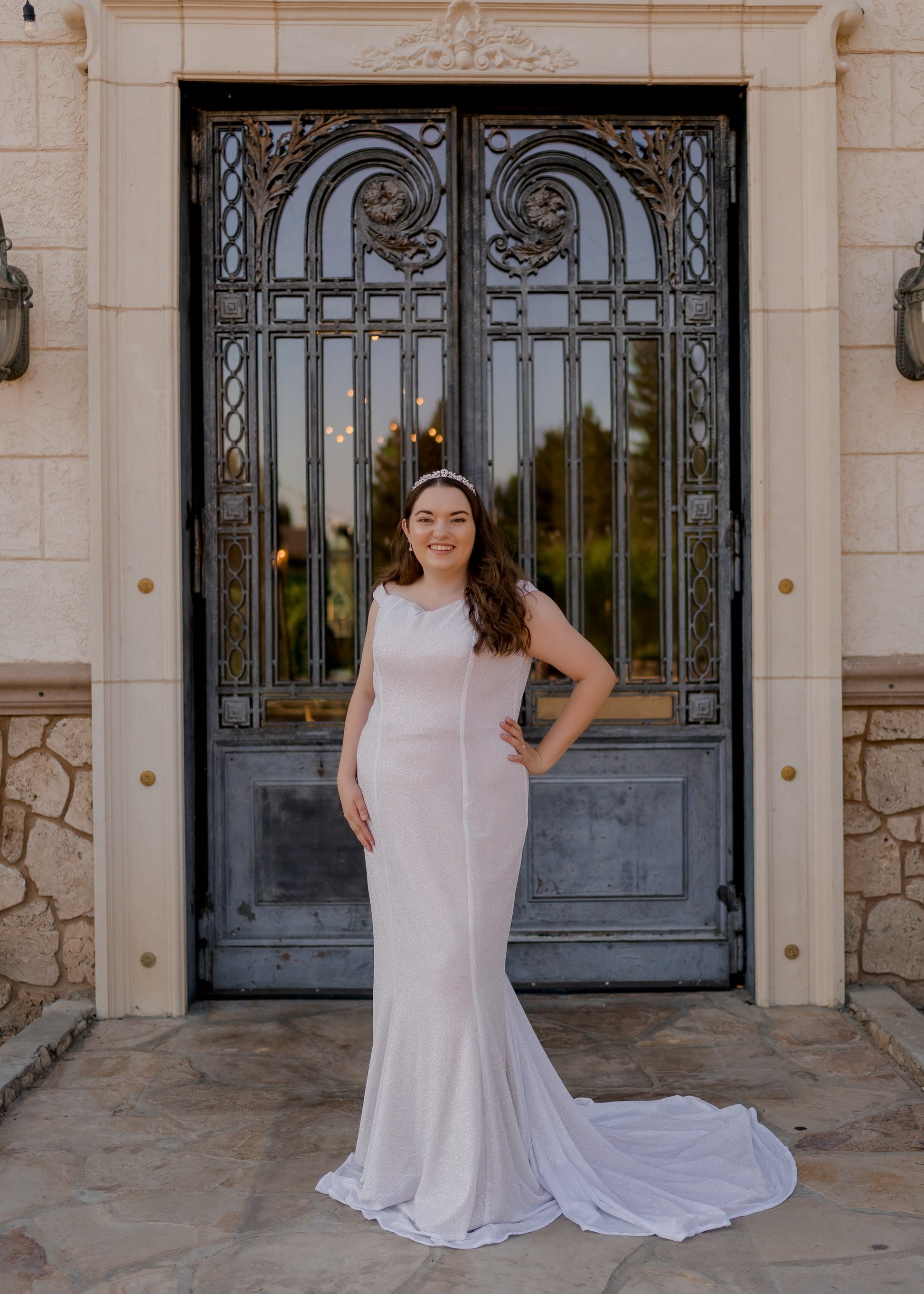 Front view of bride wearing Alora off-the-shoulder glitter trumpet wedding gown with medium-length train