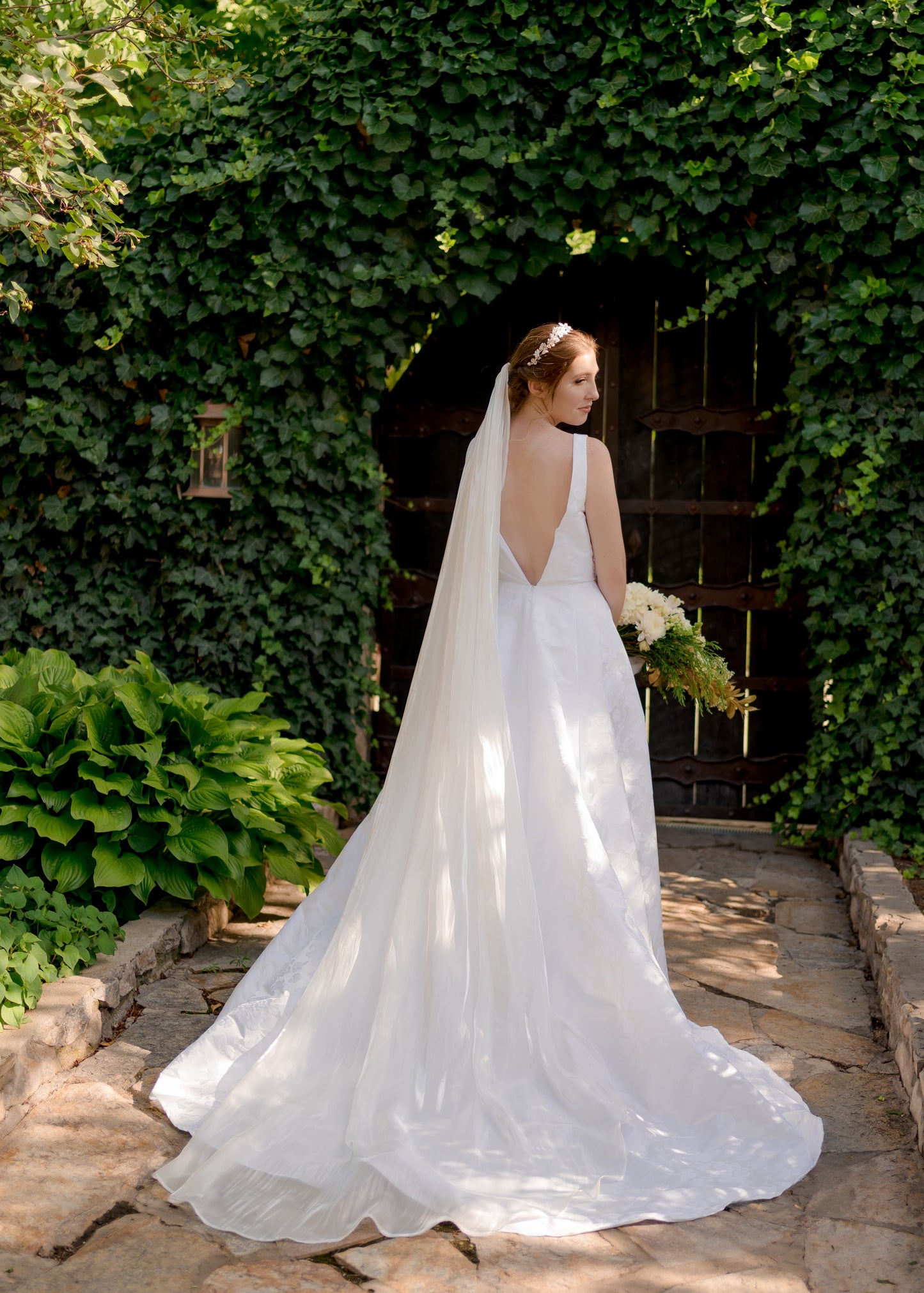 A bride wearing the flowing organza bridal veil, cara, with fluid movement and a clean edge as it flows behind the bride. It is styled here with our Madison gown.