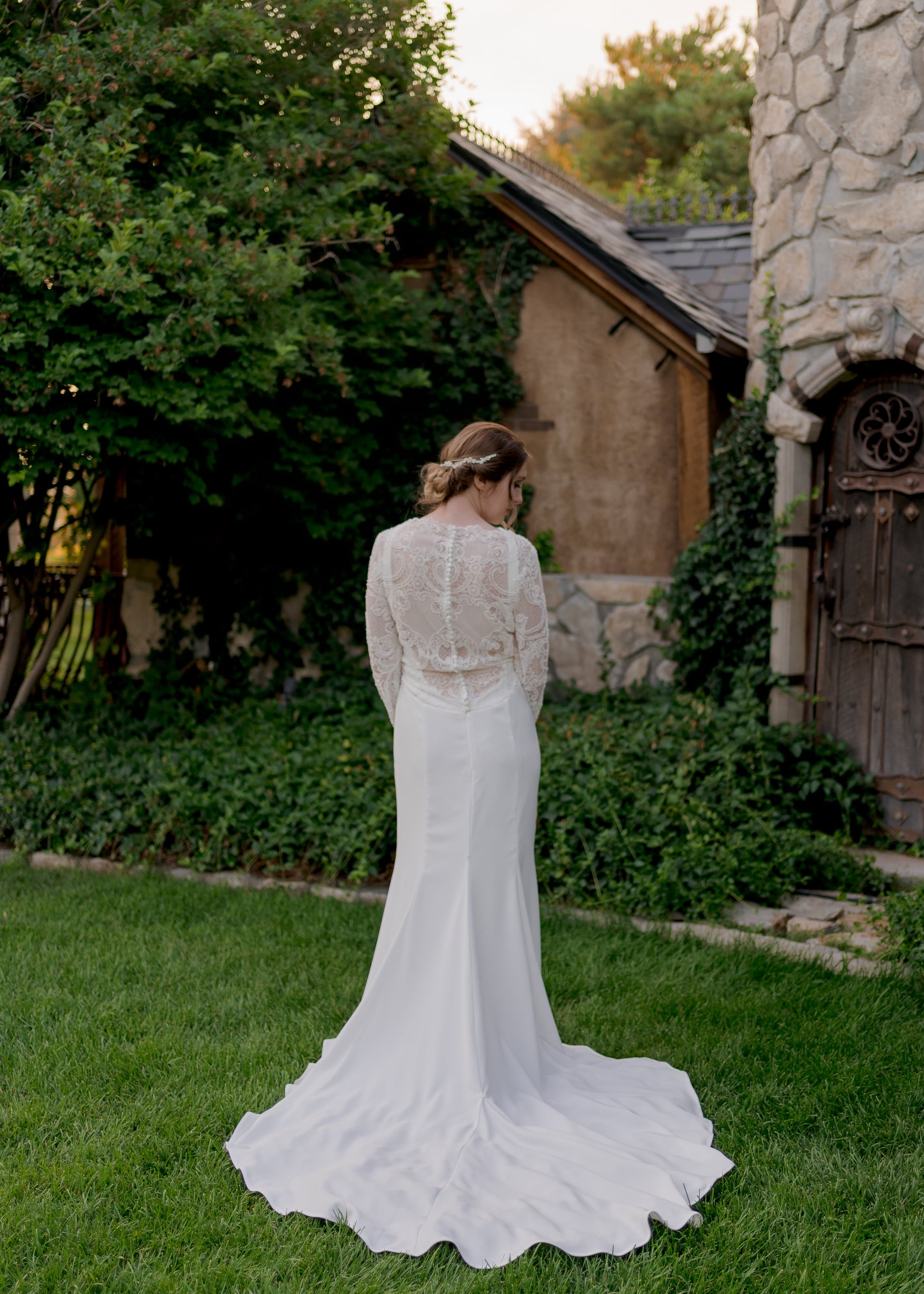 A full length back shot of the Zuri bridal dress on a model; the lace bodice and low scoop back show off the Stretch crepe mermaid skirt with 20-inch train and godet flare.