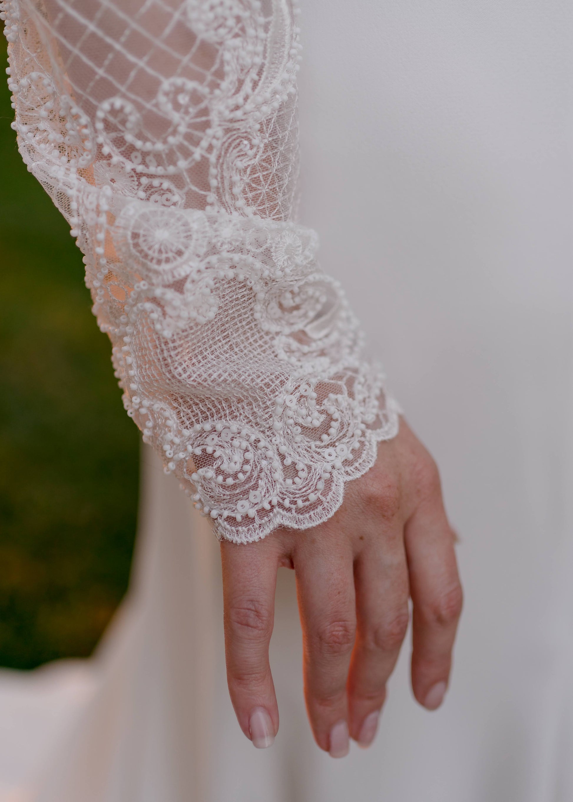 Close-up of scalloped lace edge and geometric lace design on fitted long sleeves of the Zuri Wedding dress.
