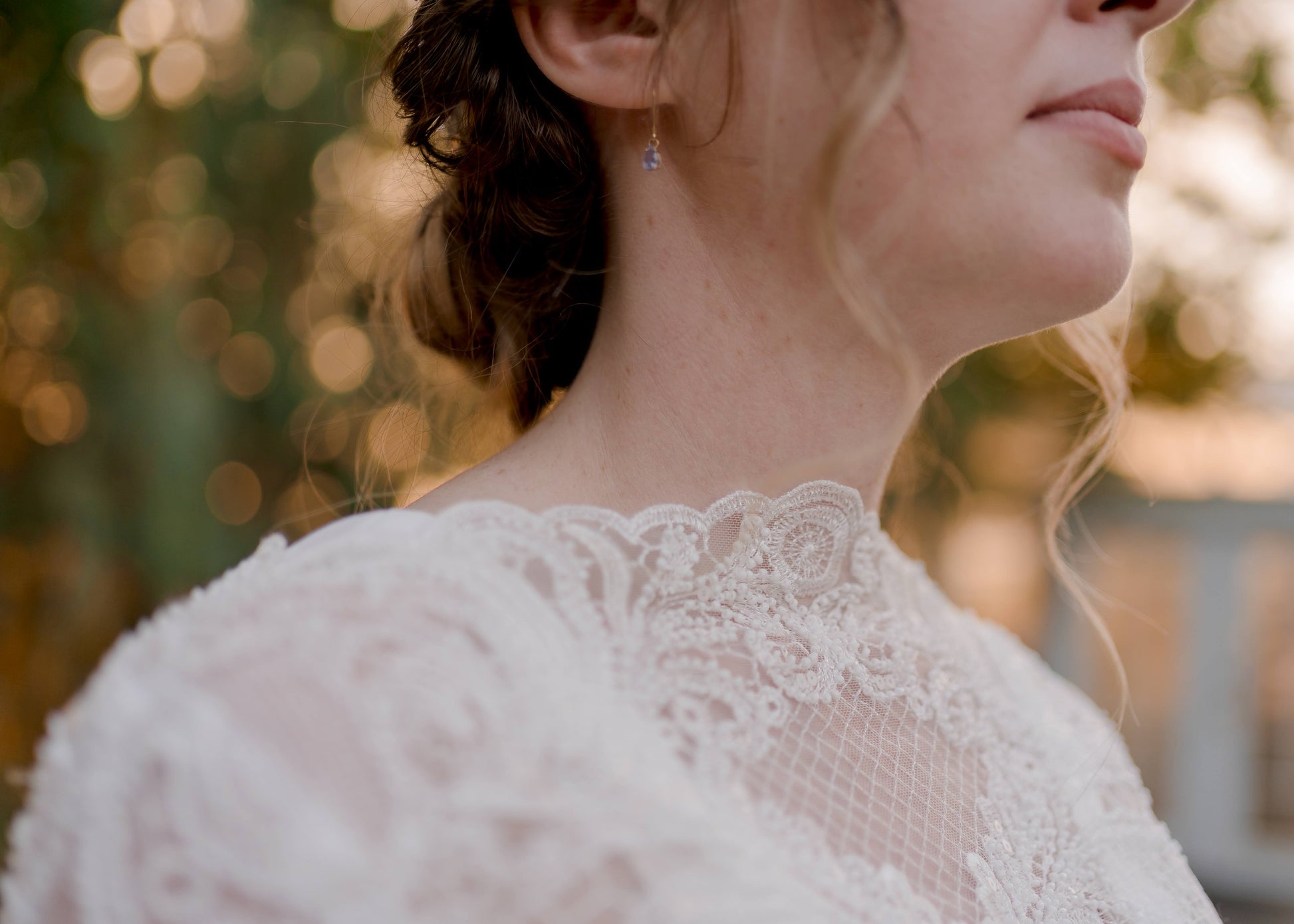 An angled miro detail shot of the scalloped mock neck with scroll lace and beading of the Zuri gown.