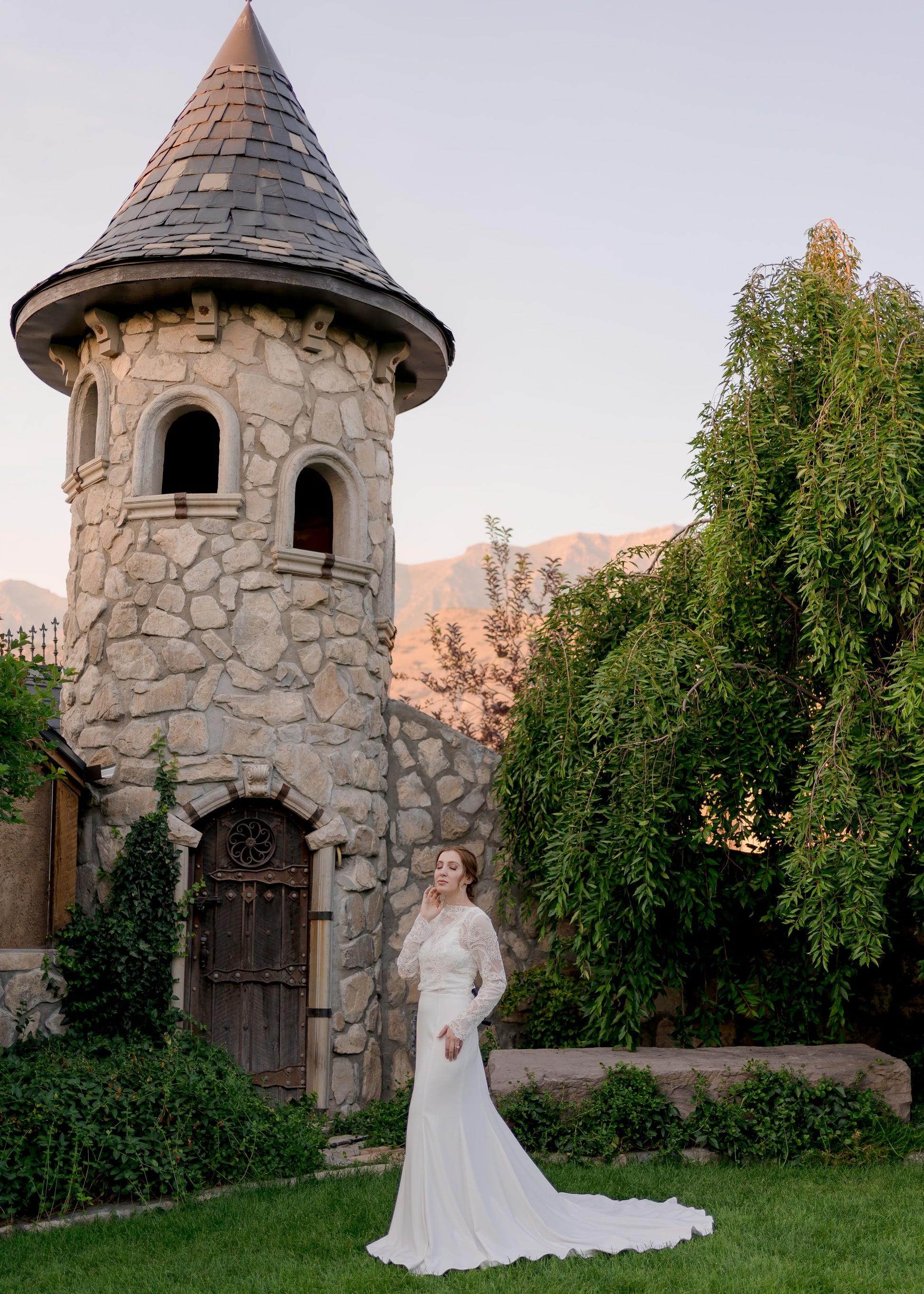 A ¾ angled full length view of the Zuri gown from a slight distance. The crepe gown is fitted through the bodice and into the hips before it flares at the knees.