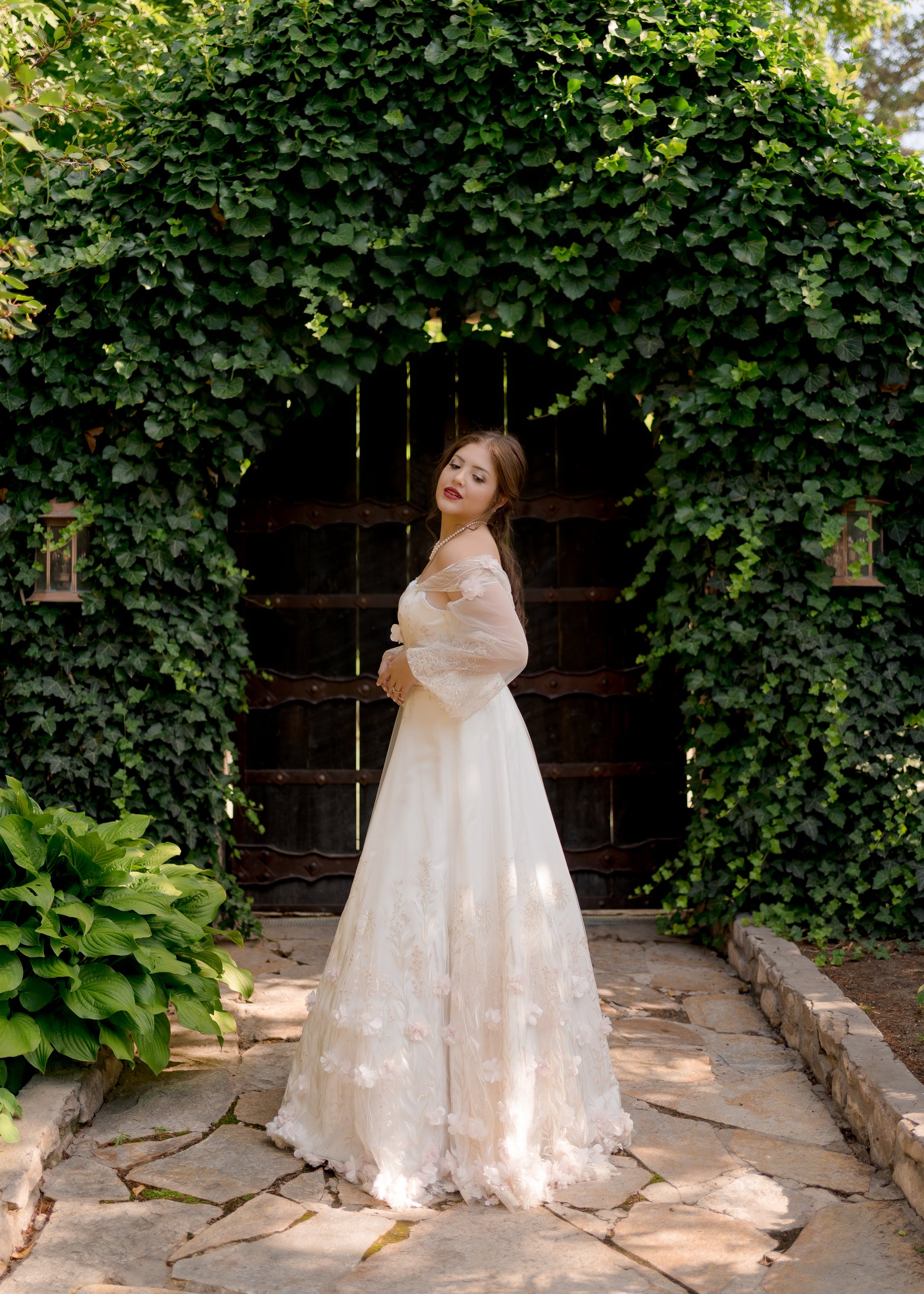 A full length image of the Prue gown from the side; The prue gown has an a-line skirt with  sweetheart neckline, bishop sleeves, and no train.