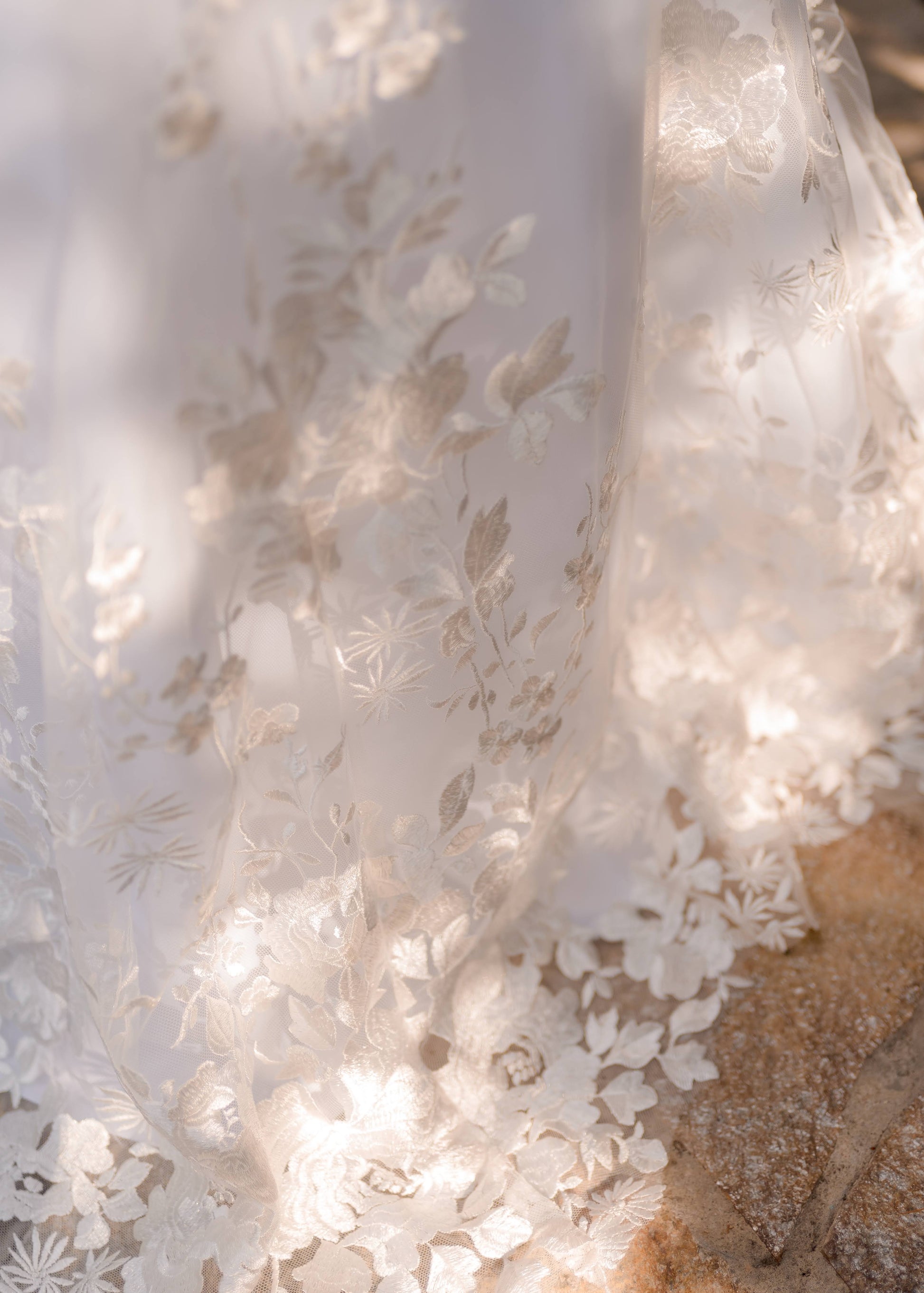 A close up of the hem of the violet gown; Flat floral lace with clusters and botanical pattern with a natural lace edge