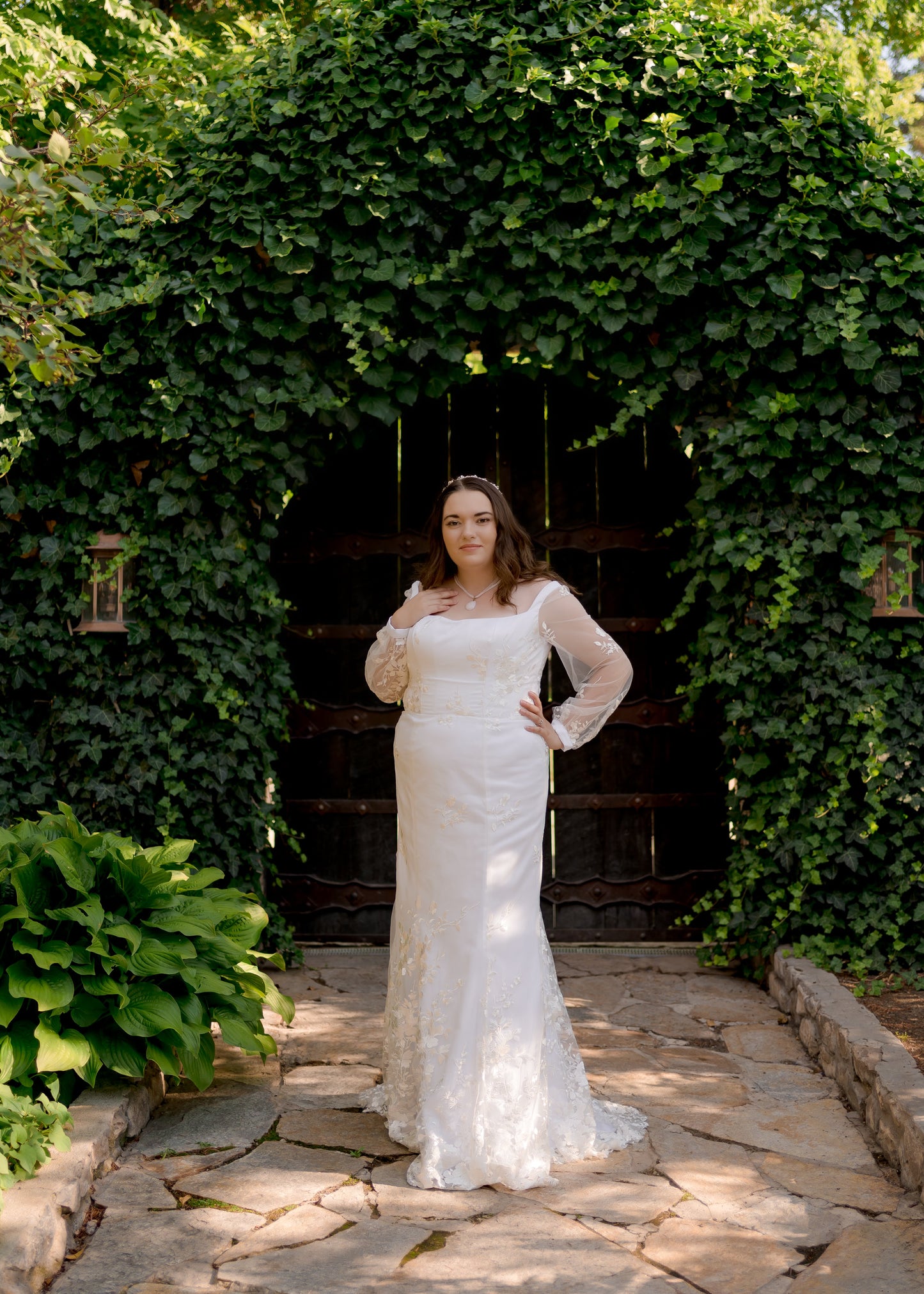 A full length image of the Violet wedding gown, showing off the gowns fit, sheer bishop sleeves, and square neckline.