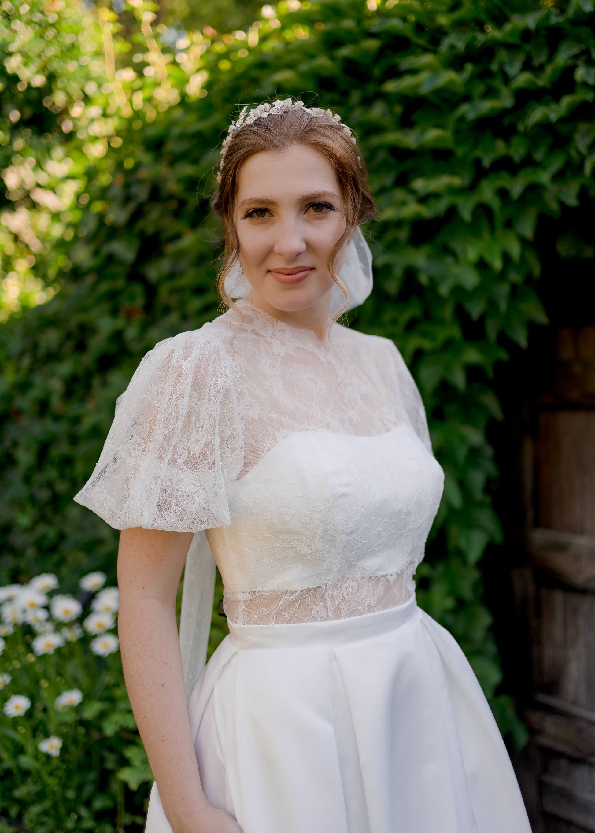 A bride wears the Jessa gown and tess bridal bow; she looks into the camera with the bow poking out behind her head.