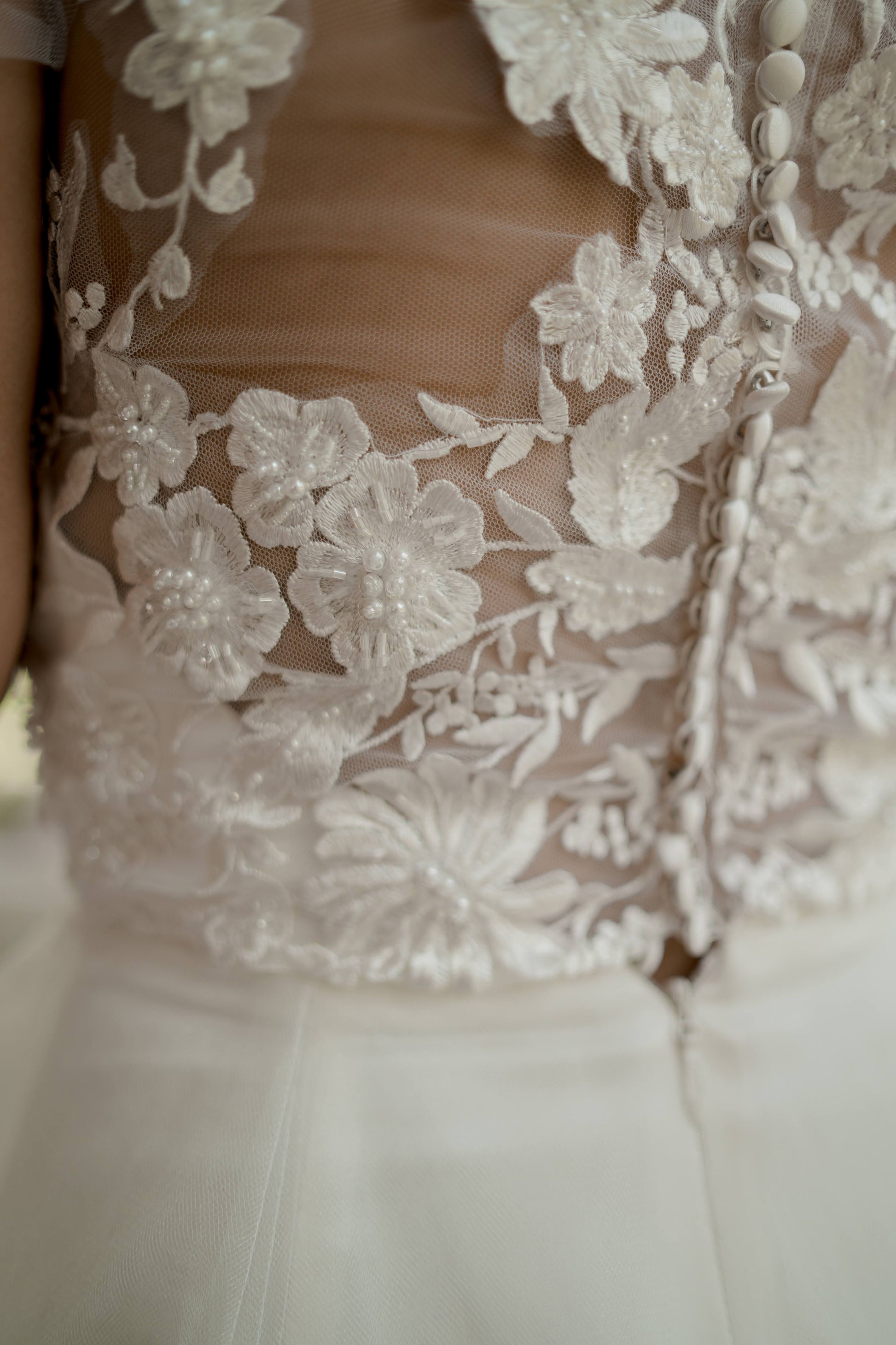 Extreme close-up of the back bodice showing intricate floral lace and delicate beadwork on the illusion tulle, capturing the craftsmanship and texture.