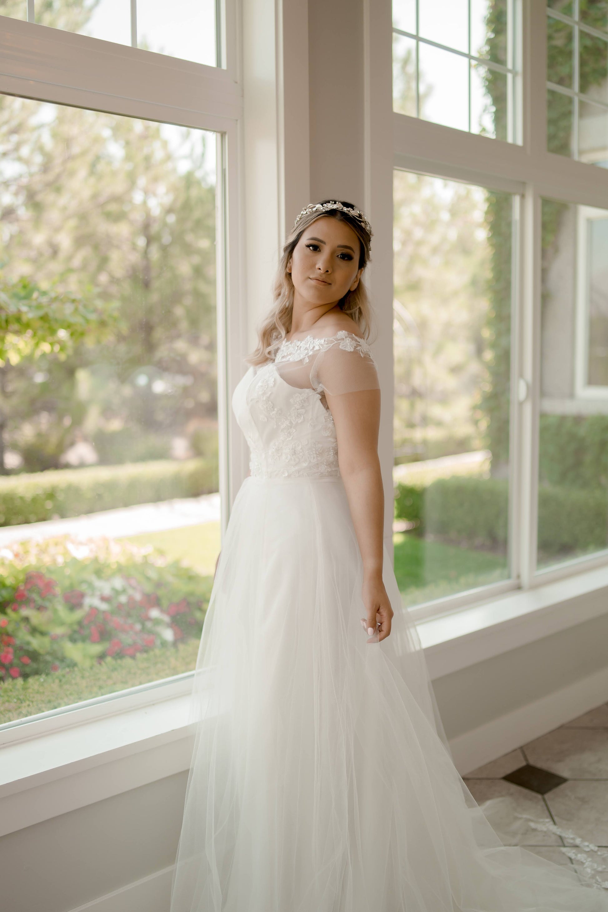 The model posed at a soft angle, turning slightly to show both the front and side of the gown, capturing the illusion neckline and A-line silhouette