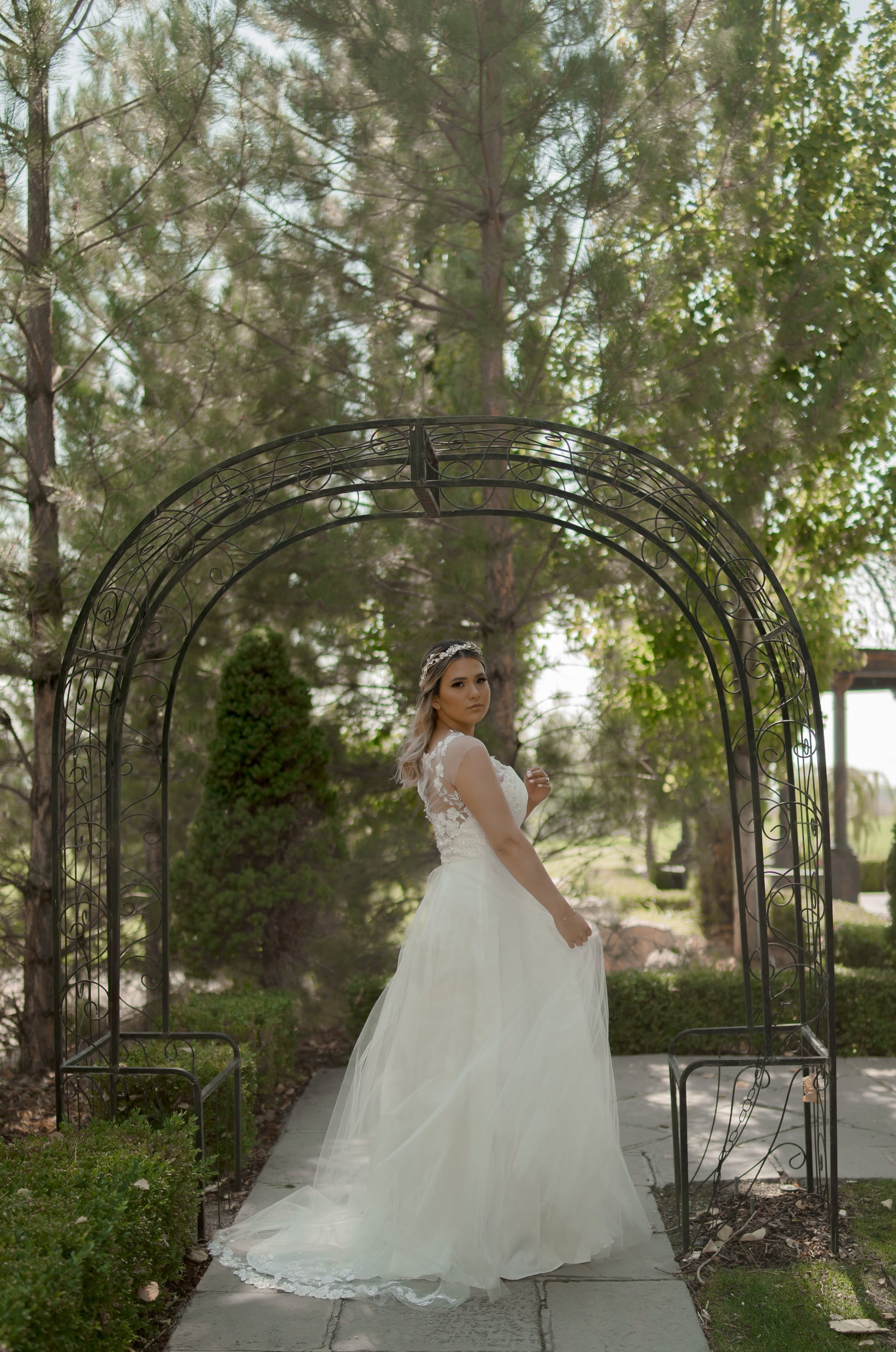 The model posed at an angle, turning over her shoulder to show  side of the gown, capturing the illusion neckline, A-line silhouette, off the shoulder tulle sleeves, and dual train.