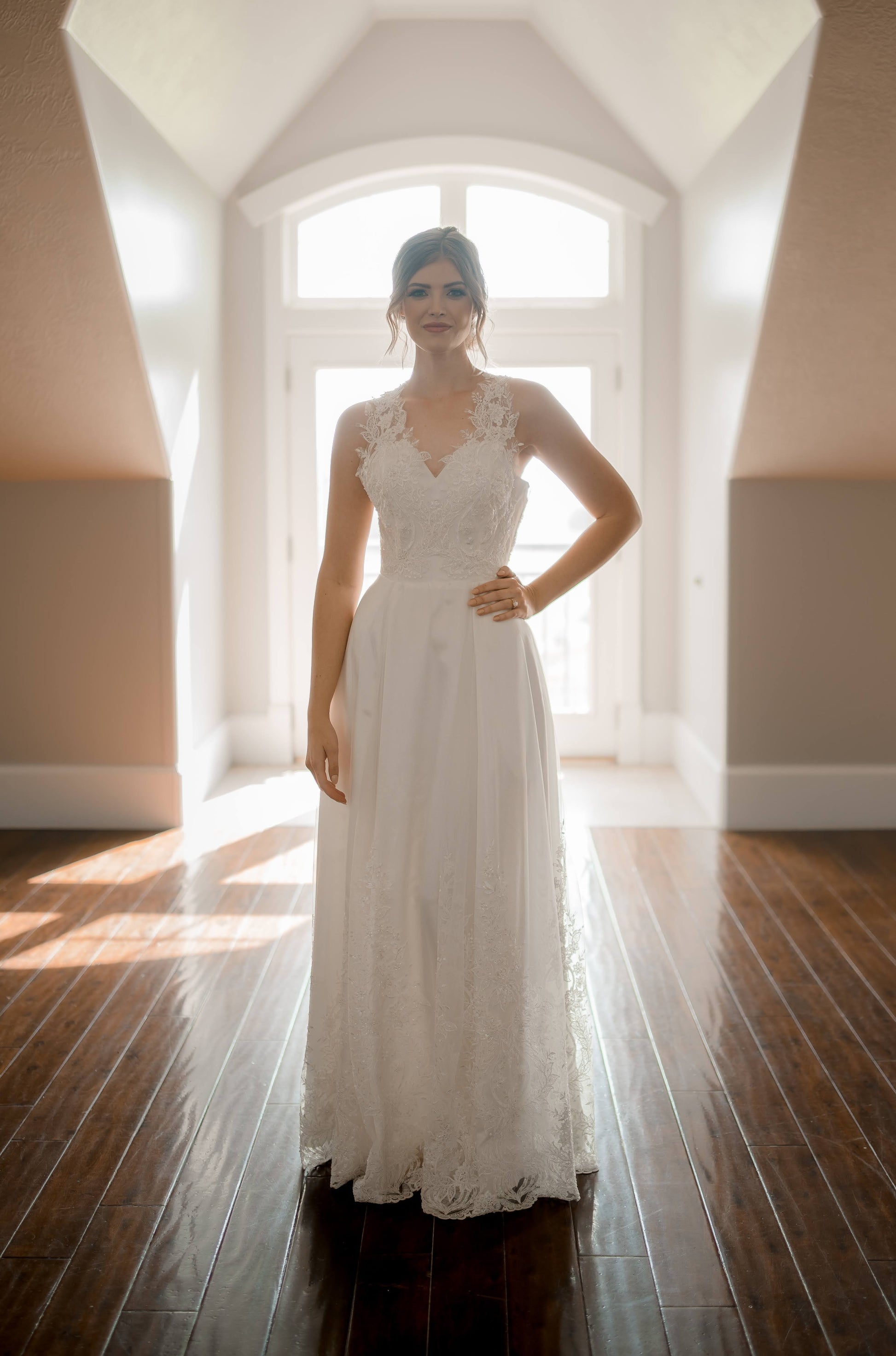A styled shoot of a bride wearing the Marie gown from the front, the modified a-line shape and lace bodice are lit from behind.