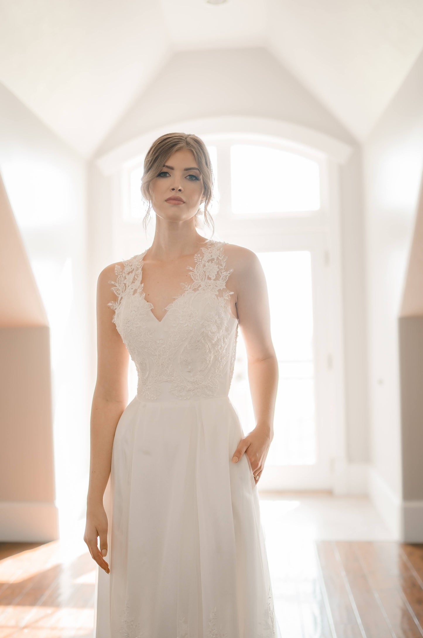 A ¾ angle shot of the marie gown on a model, she has a hand in her pocket, with the lace bodice stretching up over her shoulders.