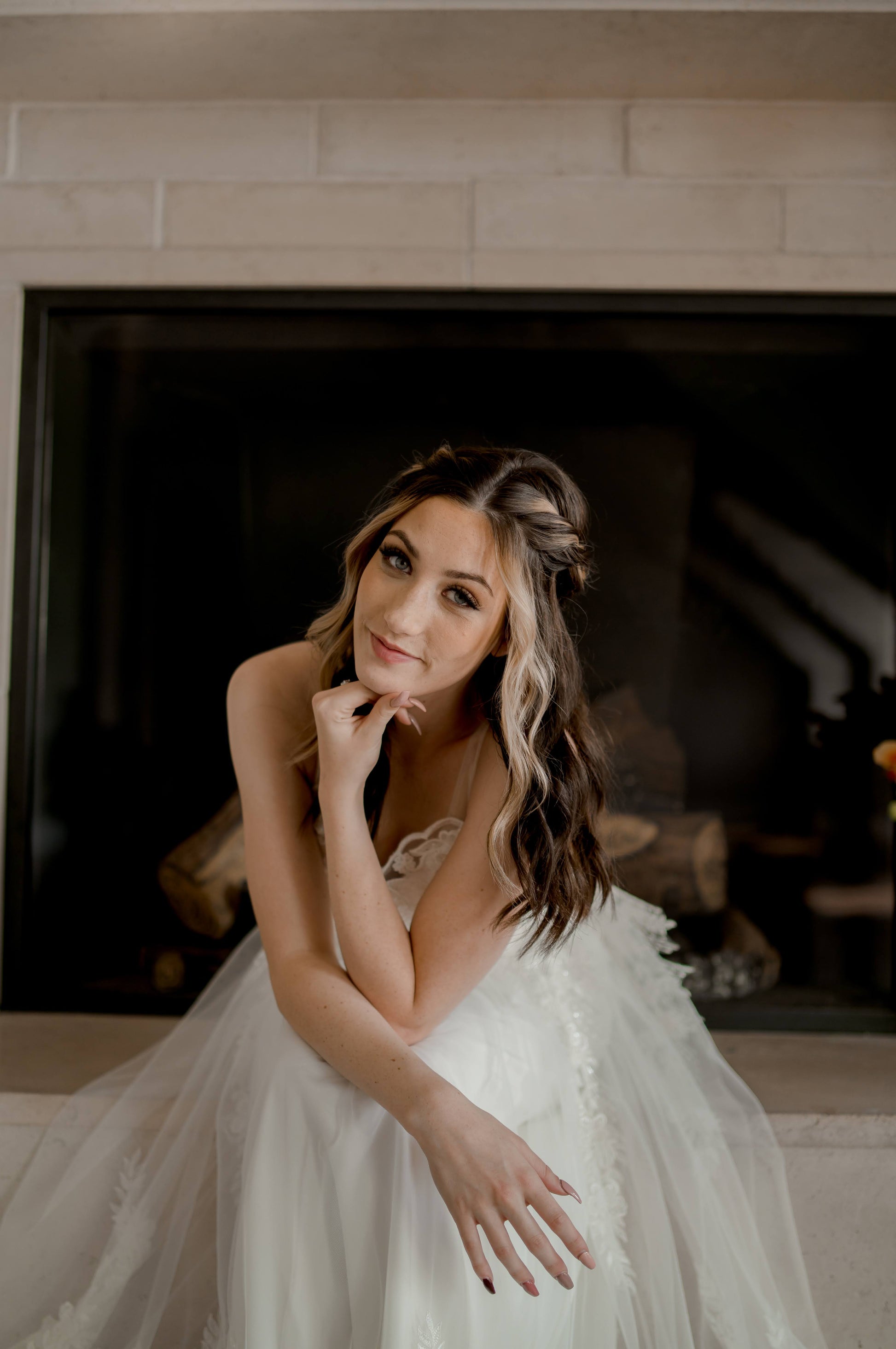 A bride sits on a fireplace leaning forward showing off the fullness in the skirt.