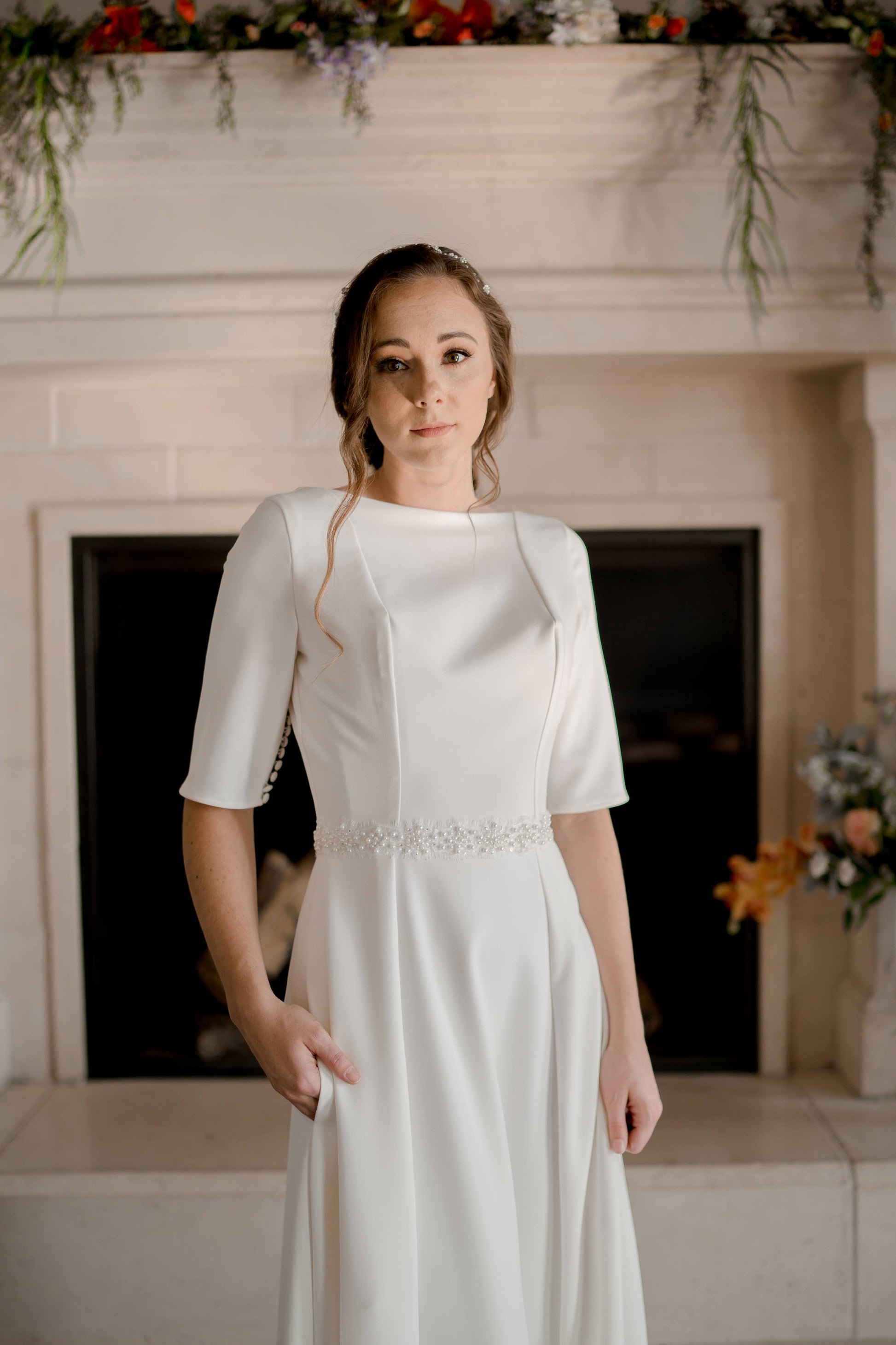 The Millie bridal belt with pearl beads paired with the Wendy dress on a model in front of a fireplace