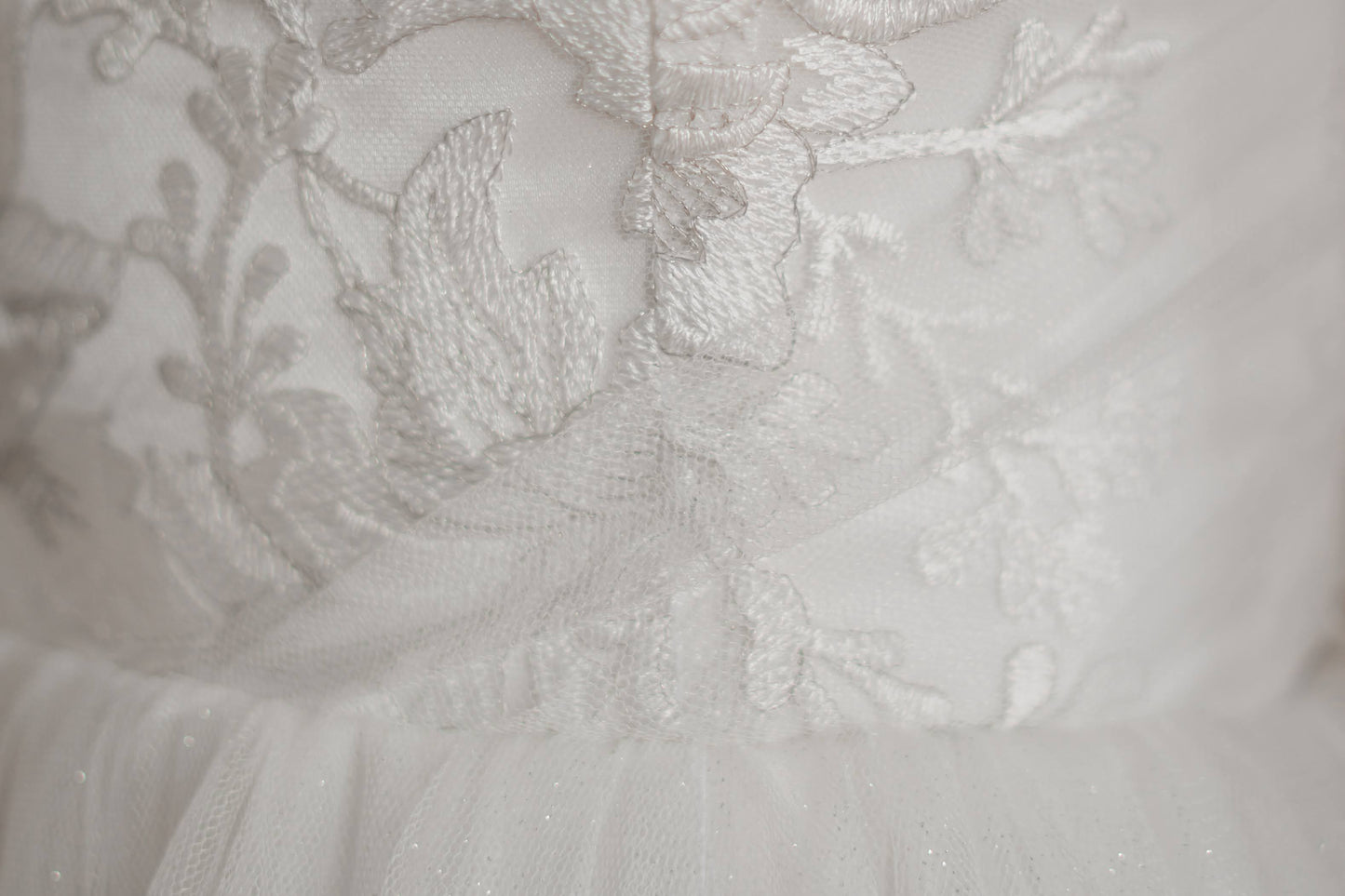 Micro detail shot of the lace on the bodie of the penelope bridal gown. In the bottom of the photo you can see the gathered skirt and small dots of silver glitter.