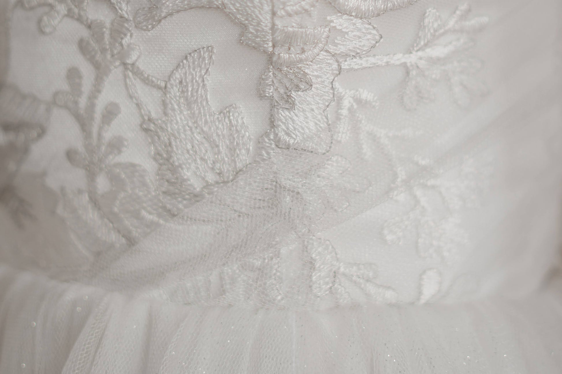 Micro detail shot of the lace on the bodie of the penelope bridal gown. In the bottom of the photo you can see the gathered skirt and small dots of silver glitter.