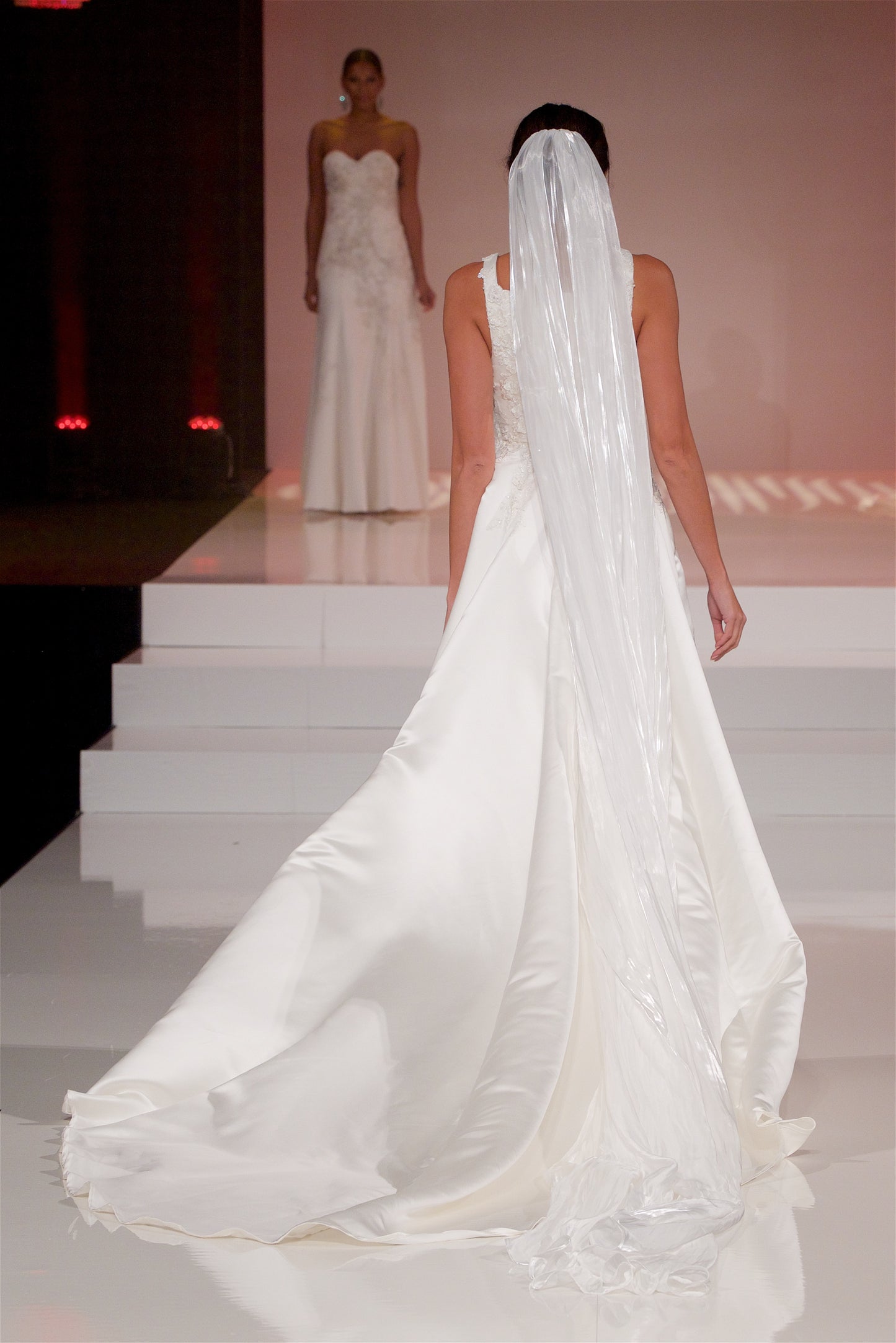 A full back veiw of the Sabina gown styled with a cathedral length Cara veil walking down a runway.