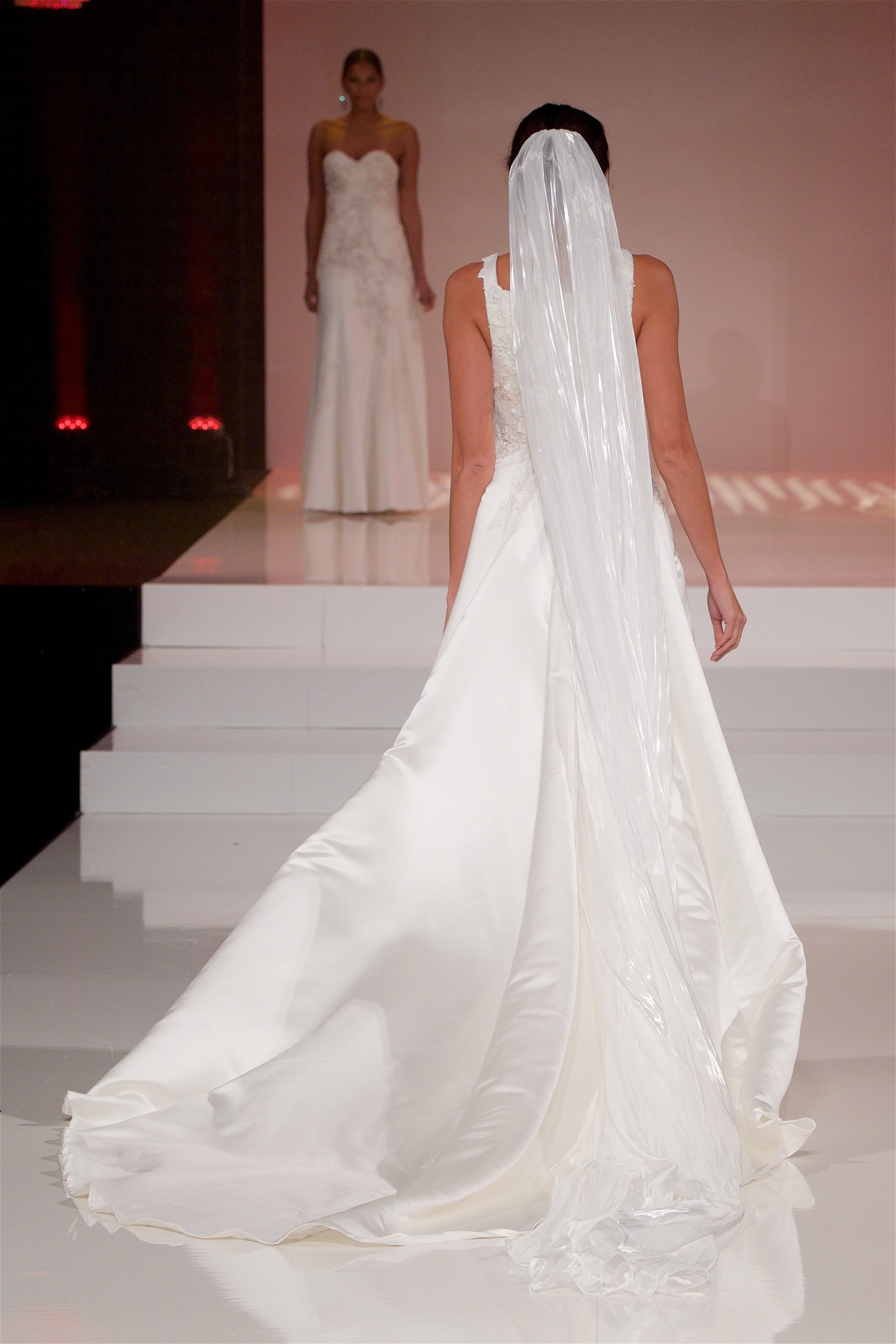 A full back veiw of the Sabina gown  styled with a cathedral length Cara veil walking down a runway.