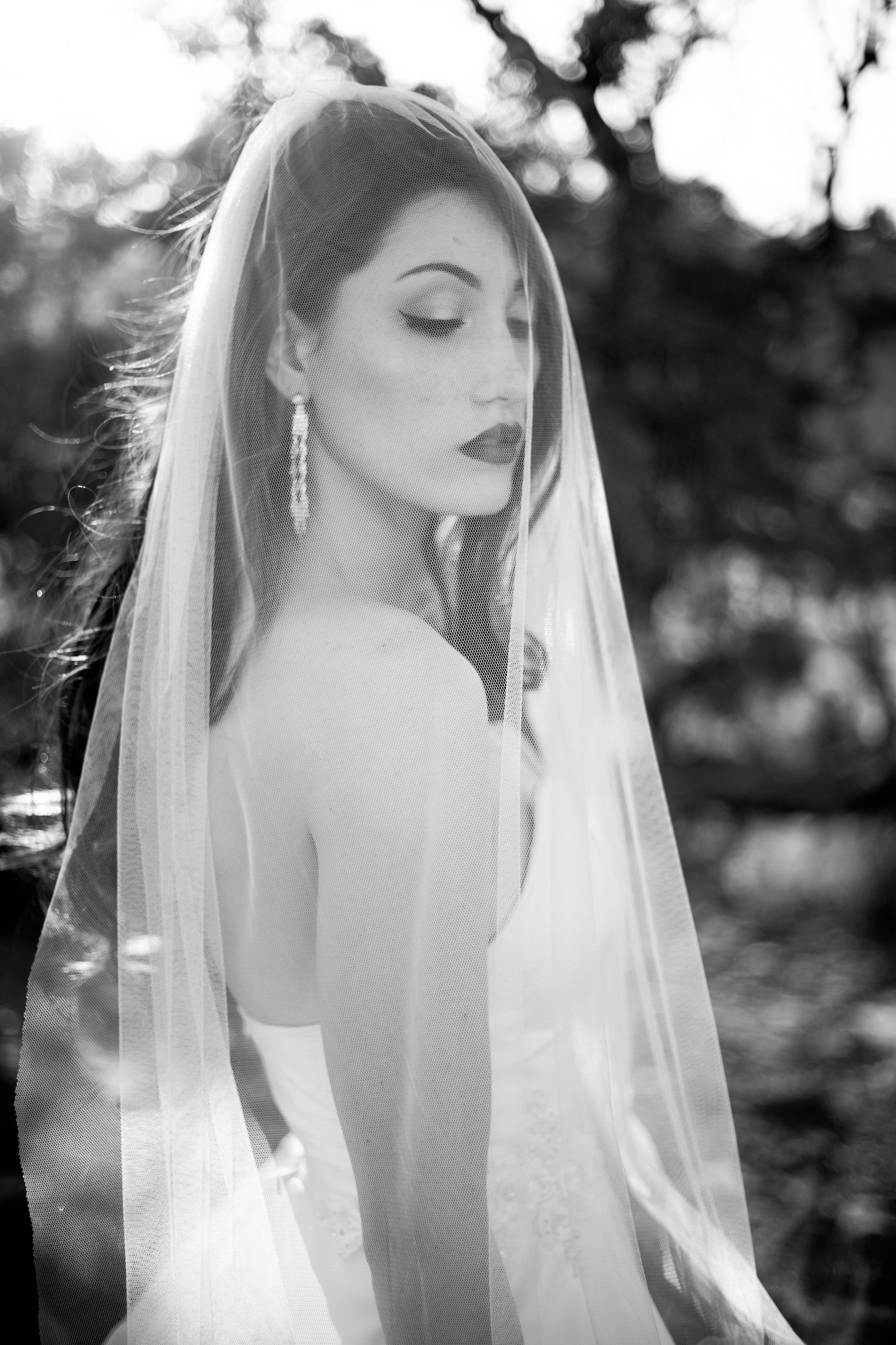A black and white photo of a bride wearing a strapless ball gown and the jane veil. The soft white tulle veil is draped over her face. 