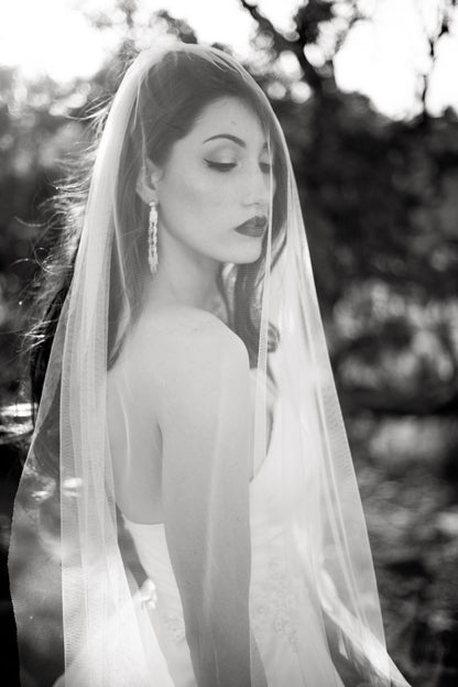 A black and white photo of a bride wearing a strapless ball gown and the jane veil. The soft white tulle veil is draped over her face. 