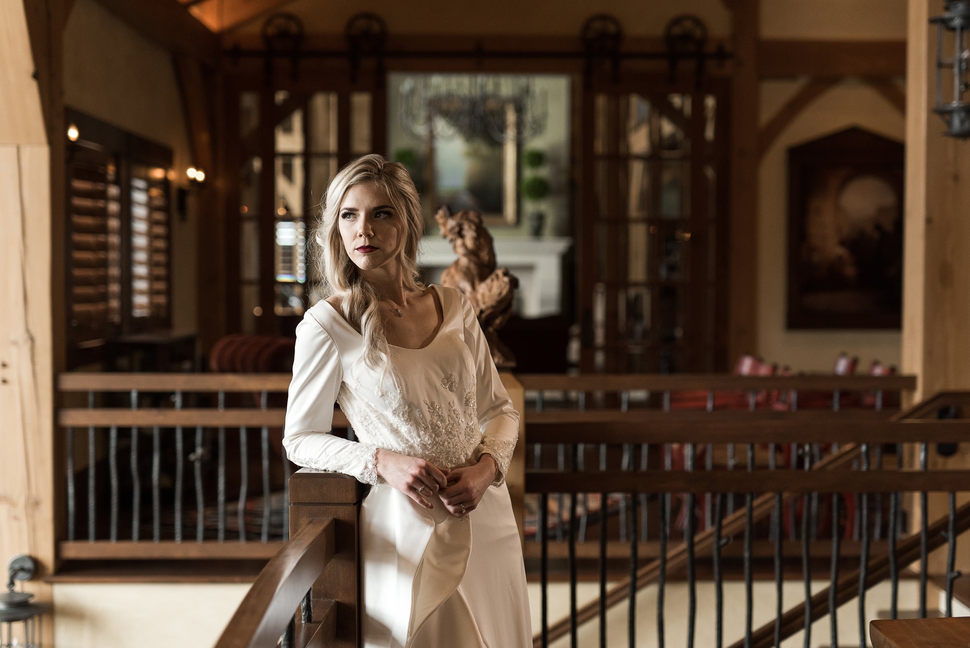 Bride leaned slightly on a railing, highlighting curved front neckline, bodice lace, and long sleeves with lace.