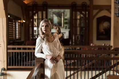 Bride leaned slightly on a railing, highlighting curved front neckline, bodice lace, and long sleeves with lace.