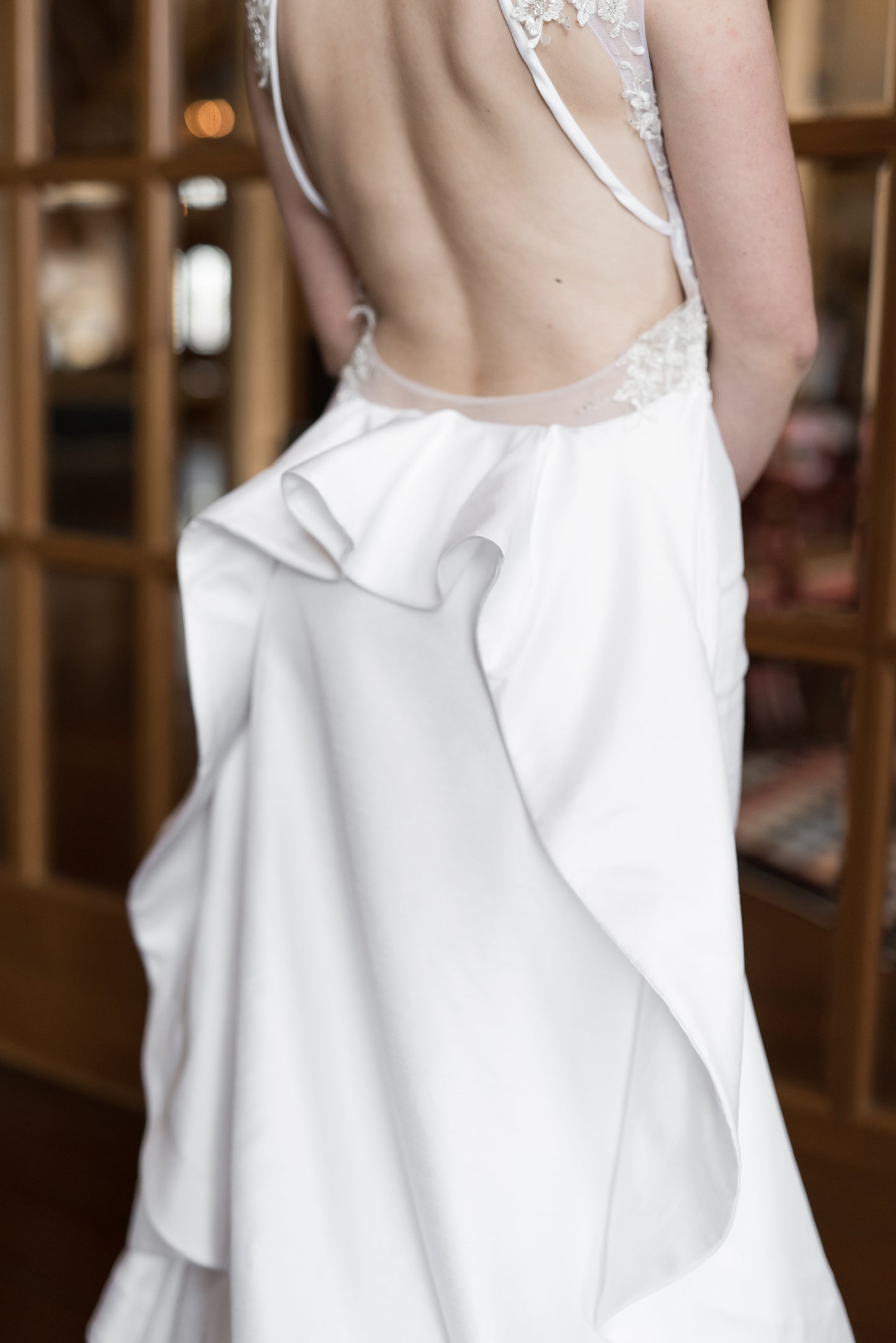 An upclose image of the ruffle on the back of Mia; a Bustle-like train with symmetrical ruffle beneath a framed keyhole made from tulle and hand placed lace. 