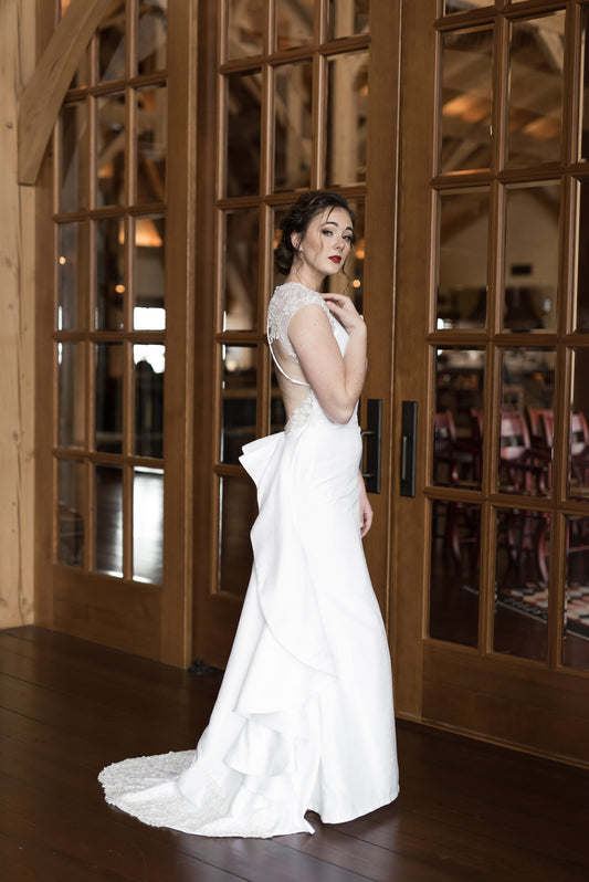 A side portrait of a bride wearing the mia gown; The keyhole tulle back bodice spreads wide enough you can easily see the edge while the ruffle on the train gives an emphasis to the curves and shows some movement. 