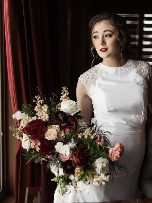 Close up of the mia gown on a model from the hips up; Shown is the Mia wedding gown with high scoop neckline and sheath silhouette.