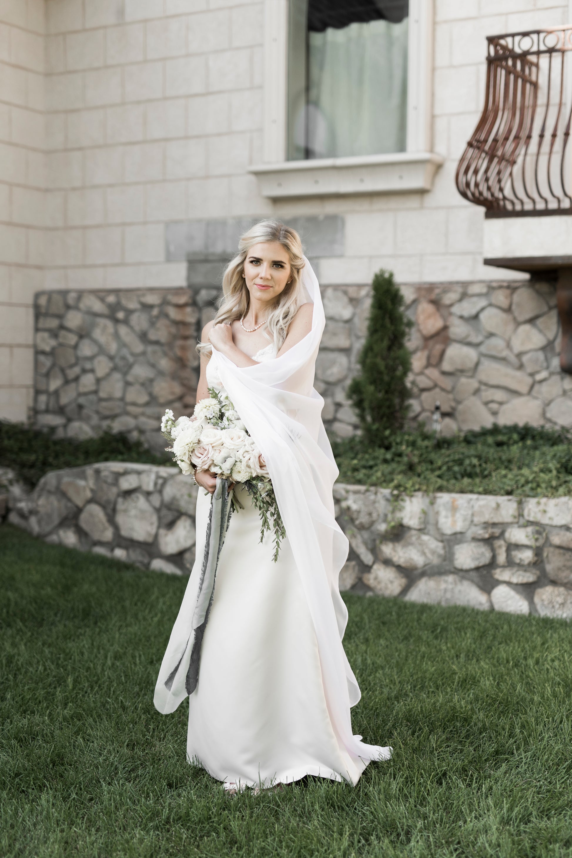 Flowing minimalist chiffon veil paired with sleek satin wedding dress; the bride wears it and has pulled it across her body showing the way the chiffon drapes. 