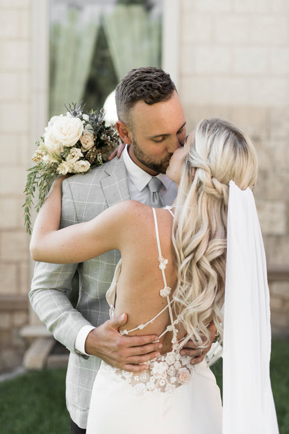 A bride leans in and kisses her hubby while she wears the chiffon veil in her hair;  the long chiffon wedding veil hangs down in a column with soft edge – Braelyn veil.