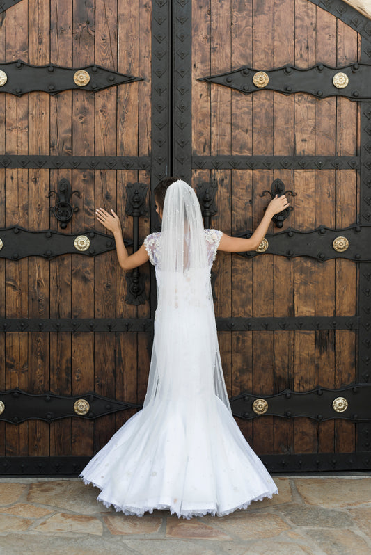 A full back view of the naomi mermaid wedding gown paired with the leah veil in puddle length for an embelished romantic look