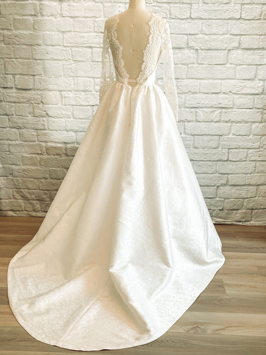 Back view of Gemma gown highlighting illusion scooped back with beaded lace scallop and flowing full skirt
