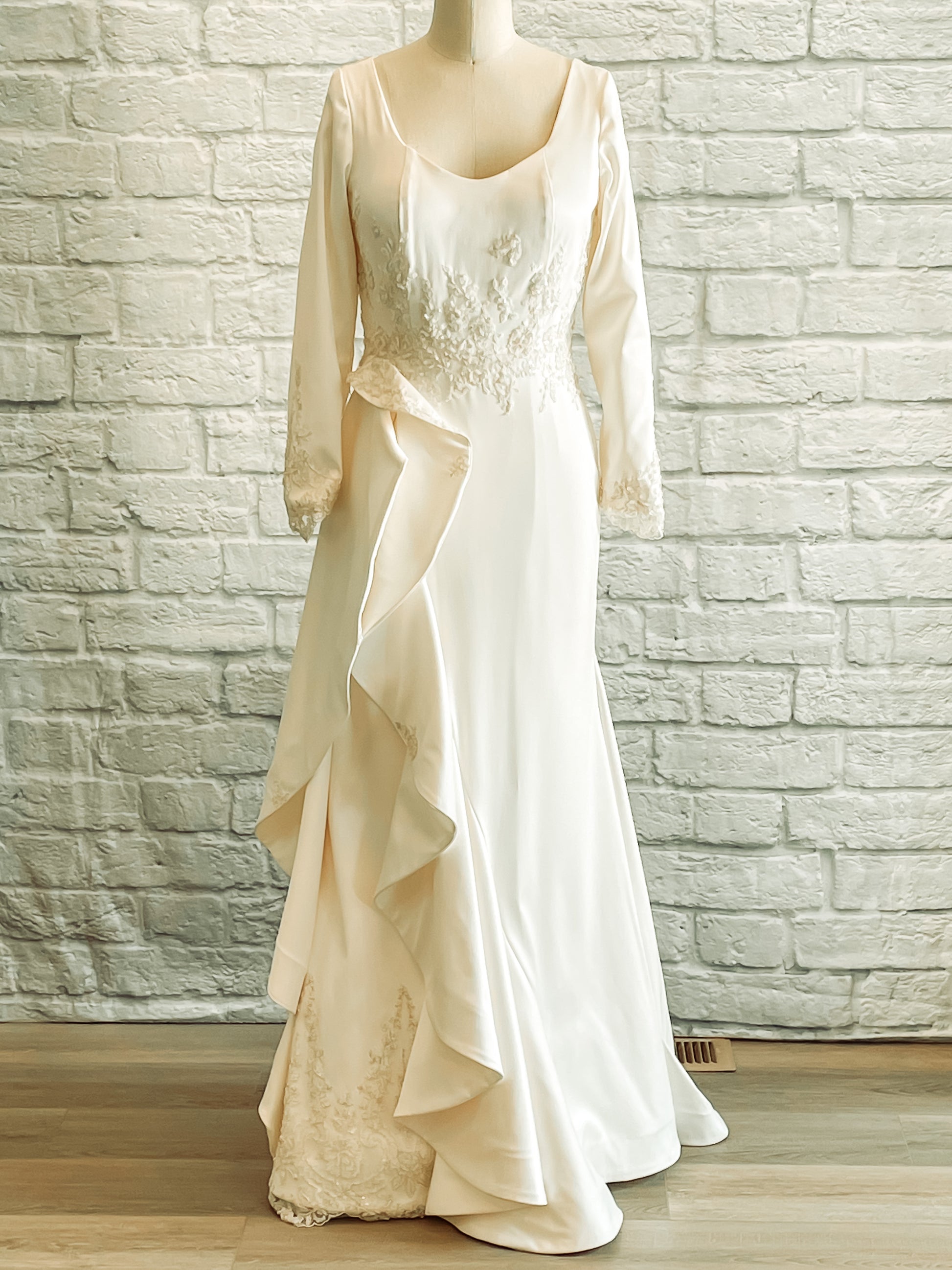 Full-length image of Emma wedding gown on mannequin, showing scoop neckline, lace waist, and ruffled asymmetric skirt.