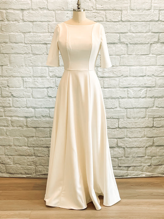 A full front view of the Wendy gown on a mannequin with a high boat neckline and clean crepe a-line silhouette.