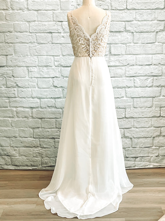 A full length back view of the winifred gown on a mannequin with Soft V-back lace overlay with satin-covered buttons and scalloped edge. The skirt has an elegant modified a-line chiffon skirt with a train. 