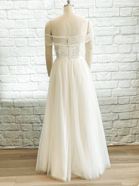 Flll back view of the penelope gown with a Curved back neckline, buttoned tulle swag, and soft skirt fall. 