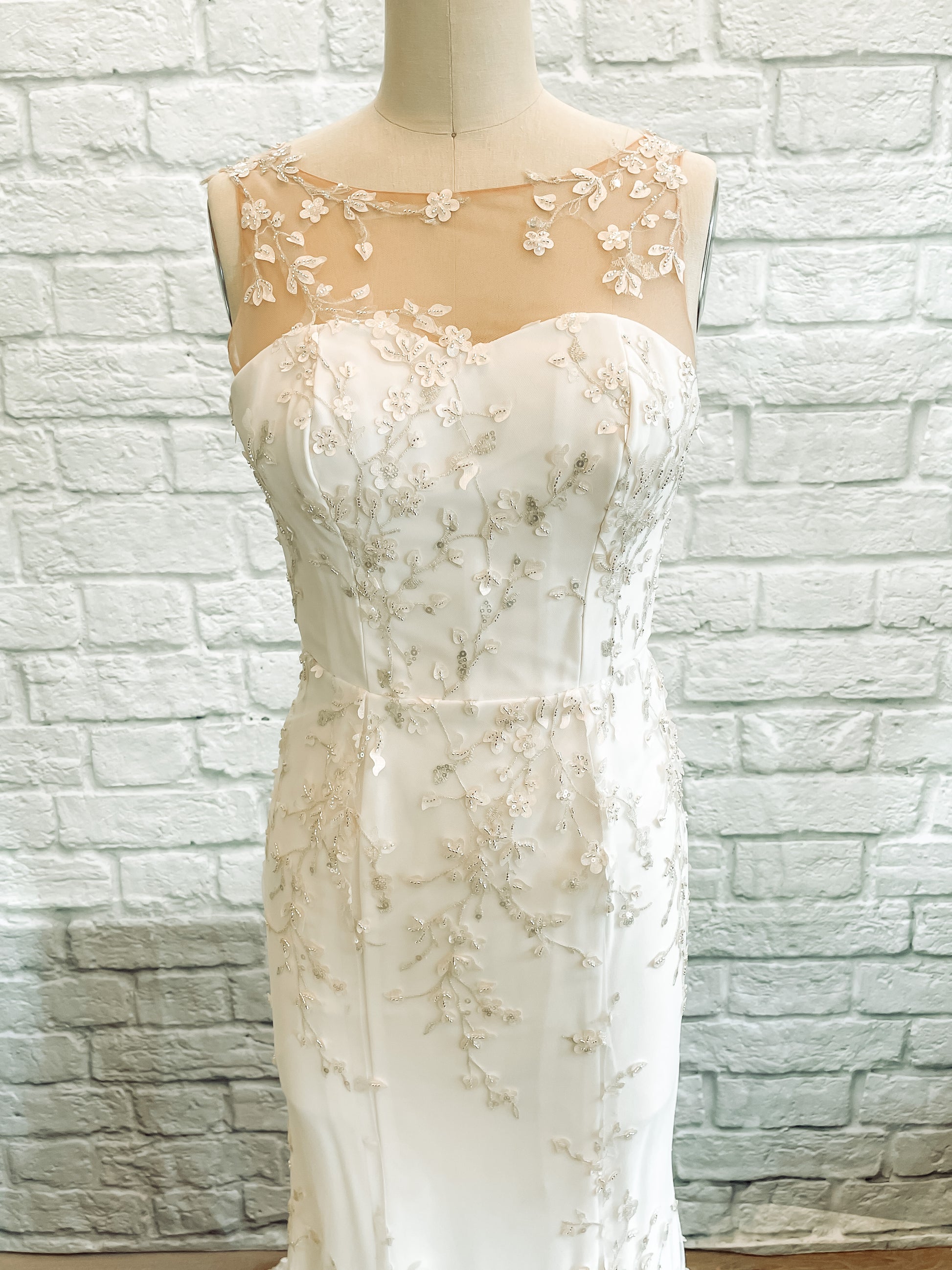 A close up bodice and top of skirt view of the lorien gown on a mannequin, showing the fitted bodice and lace overlay detail.